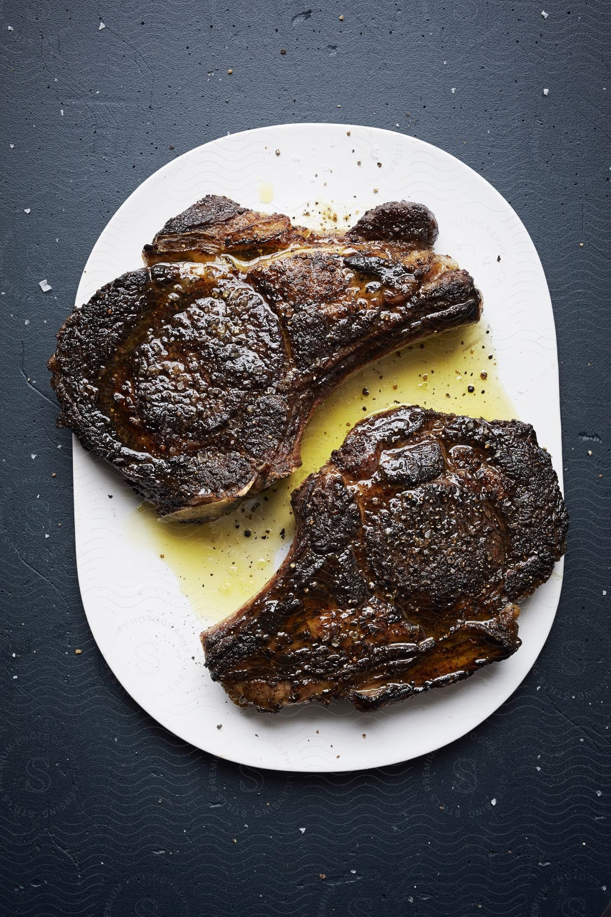Two grilled ribeye steaks on a white plate with oil