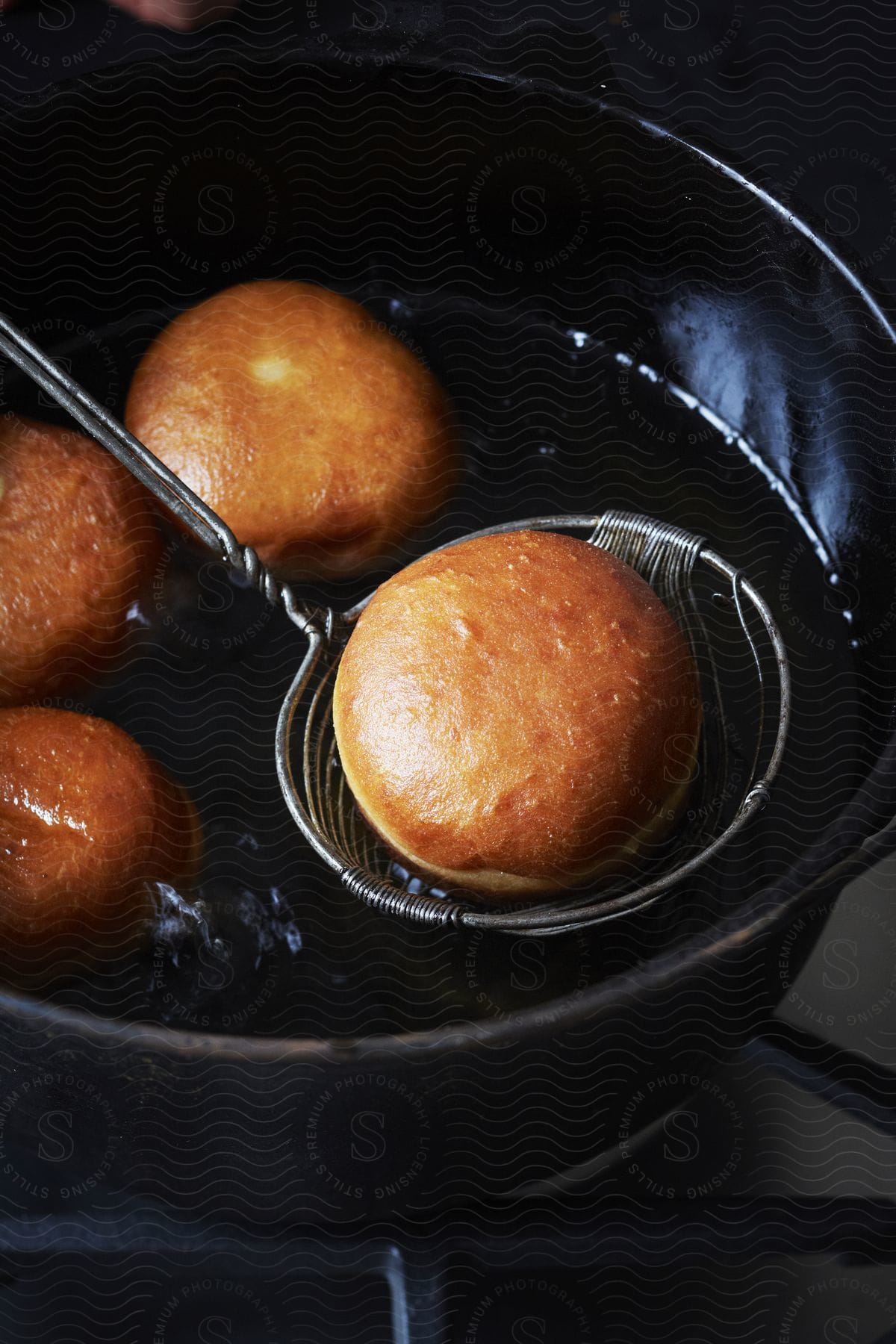 Fried brown buns being removed from a pan filled with buns and vegetable oil