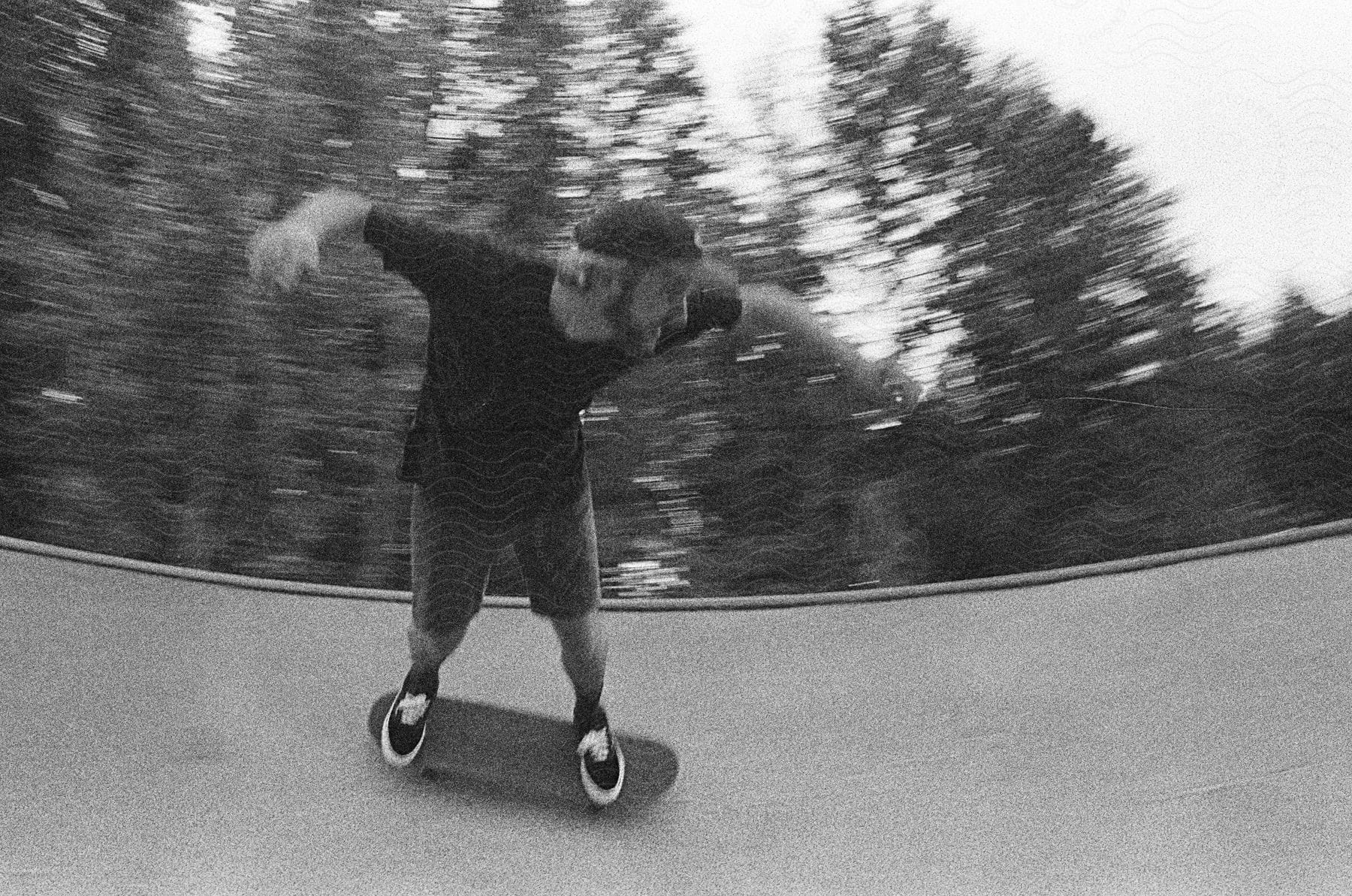 A skateboarder on a curved ramp with blurred trees in the background