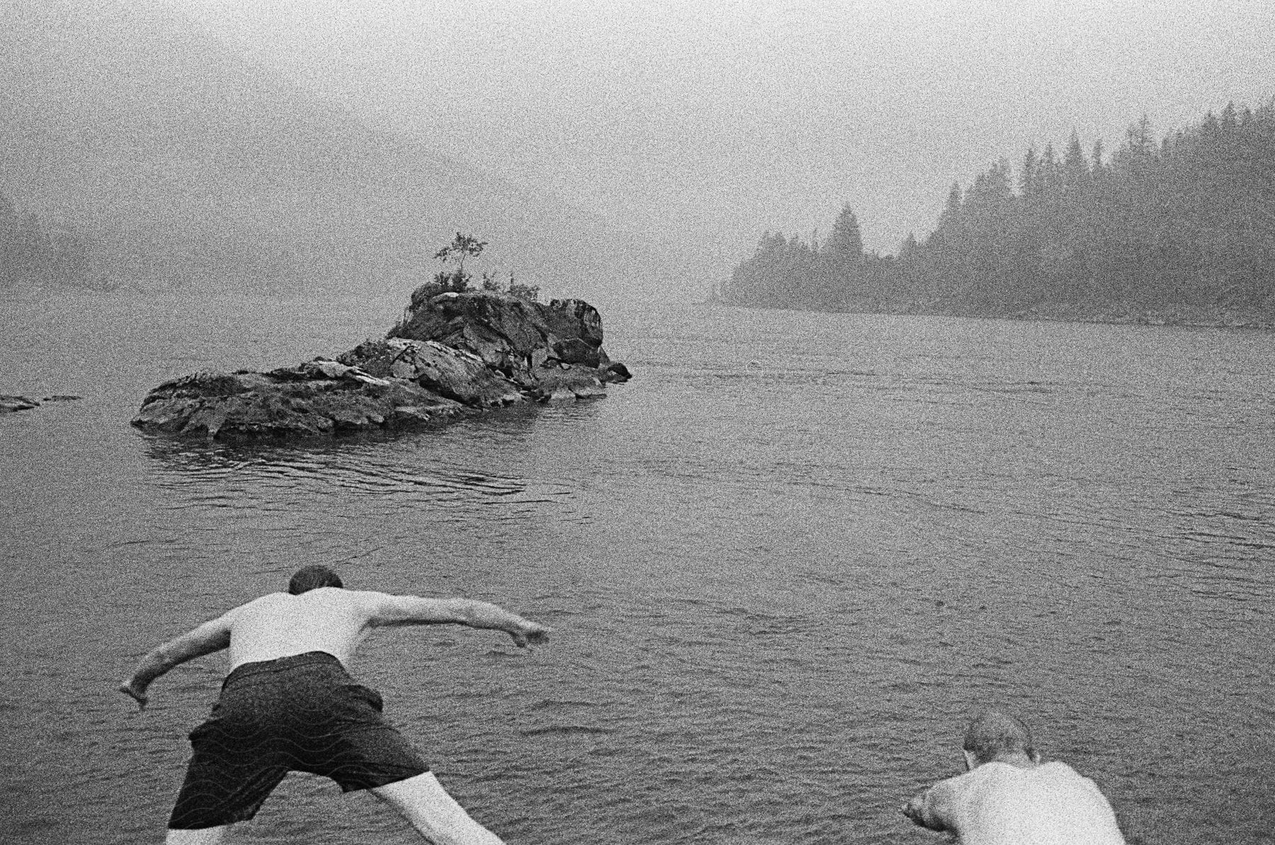 Two men leap into a lake on a sunny day