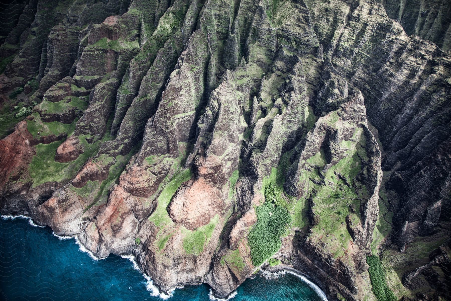 Aerial view of rocky mountains with patches of grass in a coastal region during the daytime