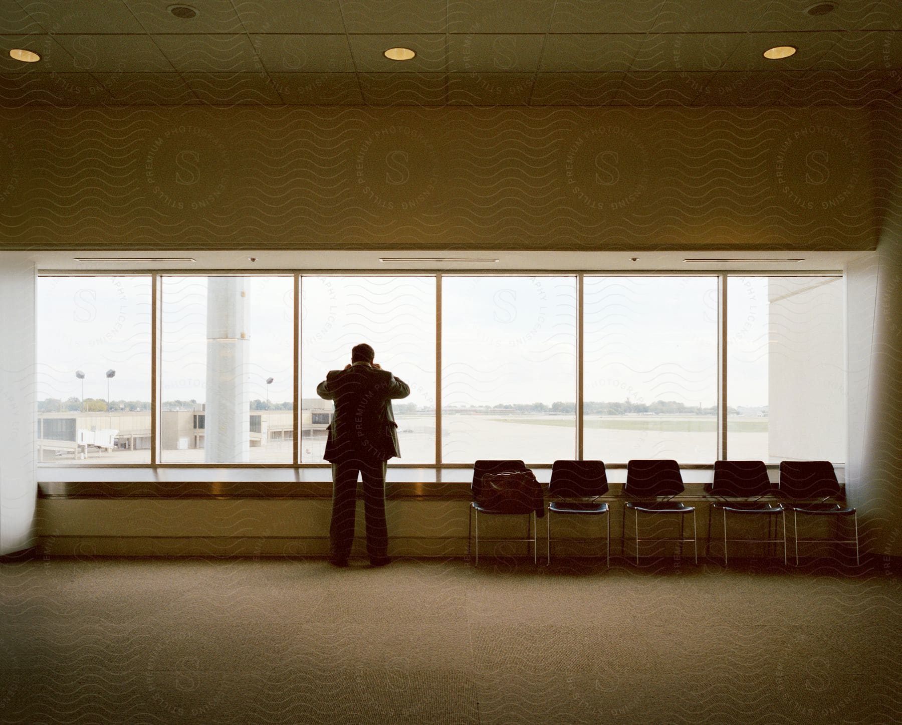 A man standing in a hall near a window with chairs beside him