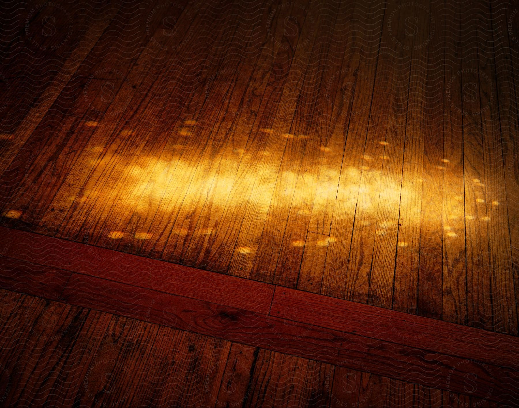 A wooden floor is lit by a beam of light creating a pattern of dancing spots