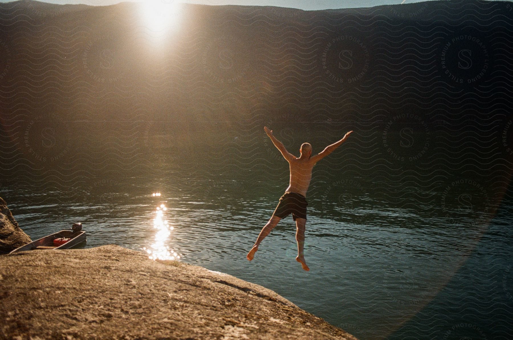 Man jumping from a dirt cliff into the water below on a sunny day