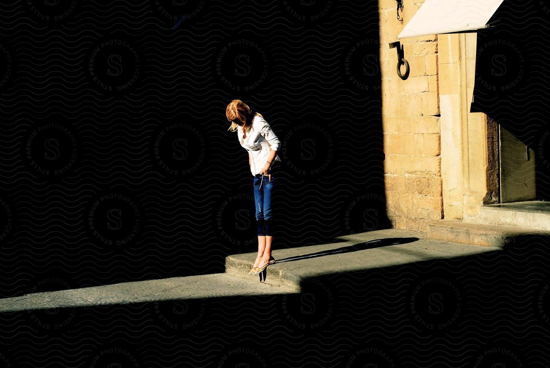 A woman standing on the curb in front of a store with the sun shining from behind a building