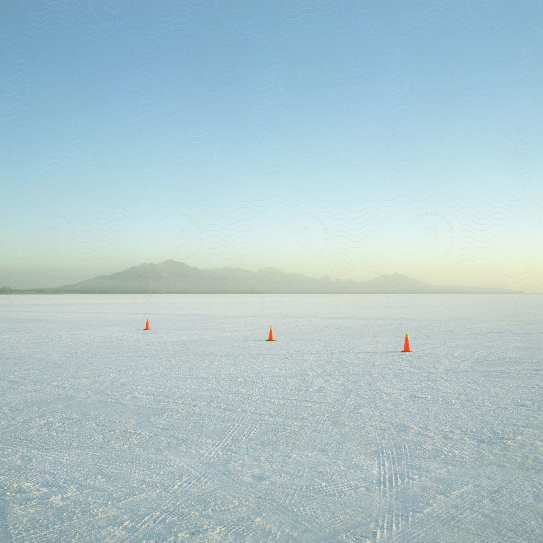 Three orange driving cones lined up in a salt flat with tire marks all over the ground