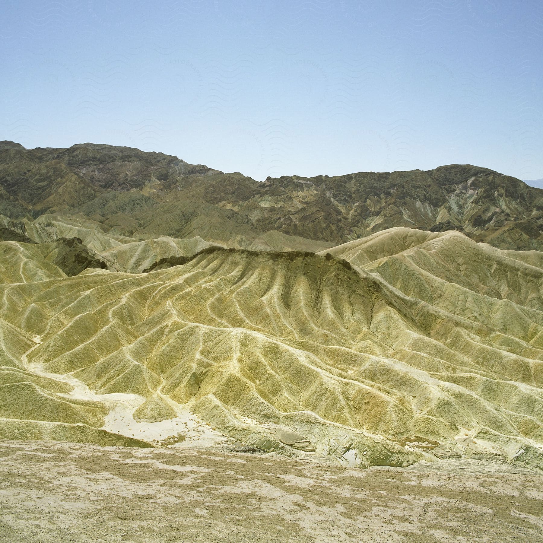 Stock photo of green hills separate arid plain from mountain under a clear blue sky