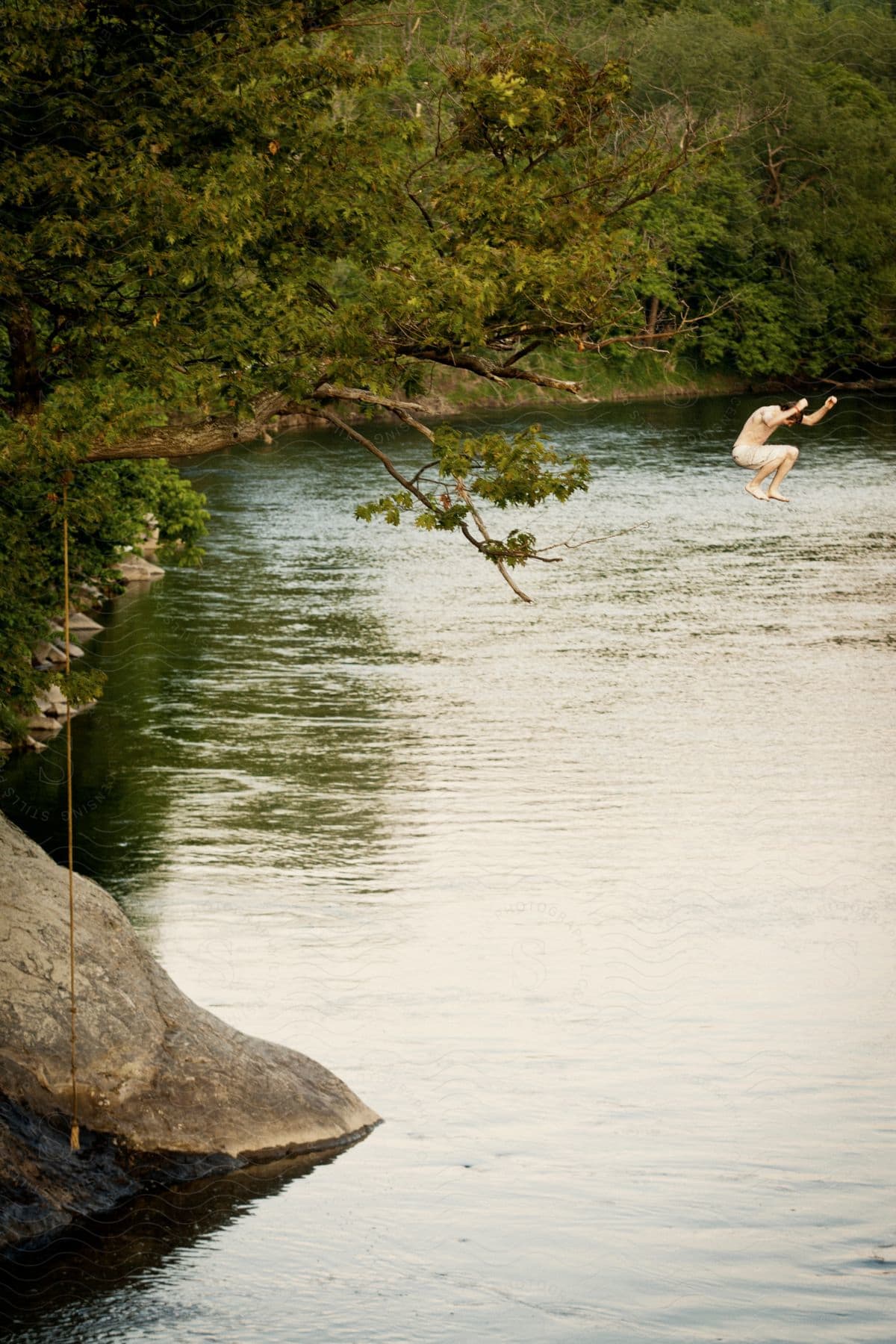 A man jumps off a cliff into a lake wearing shorts