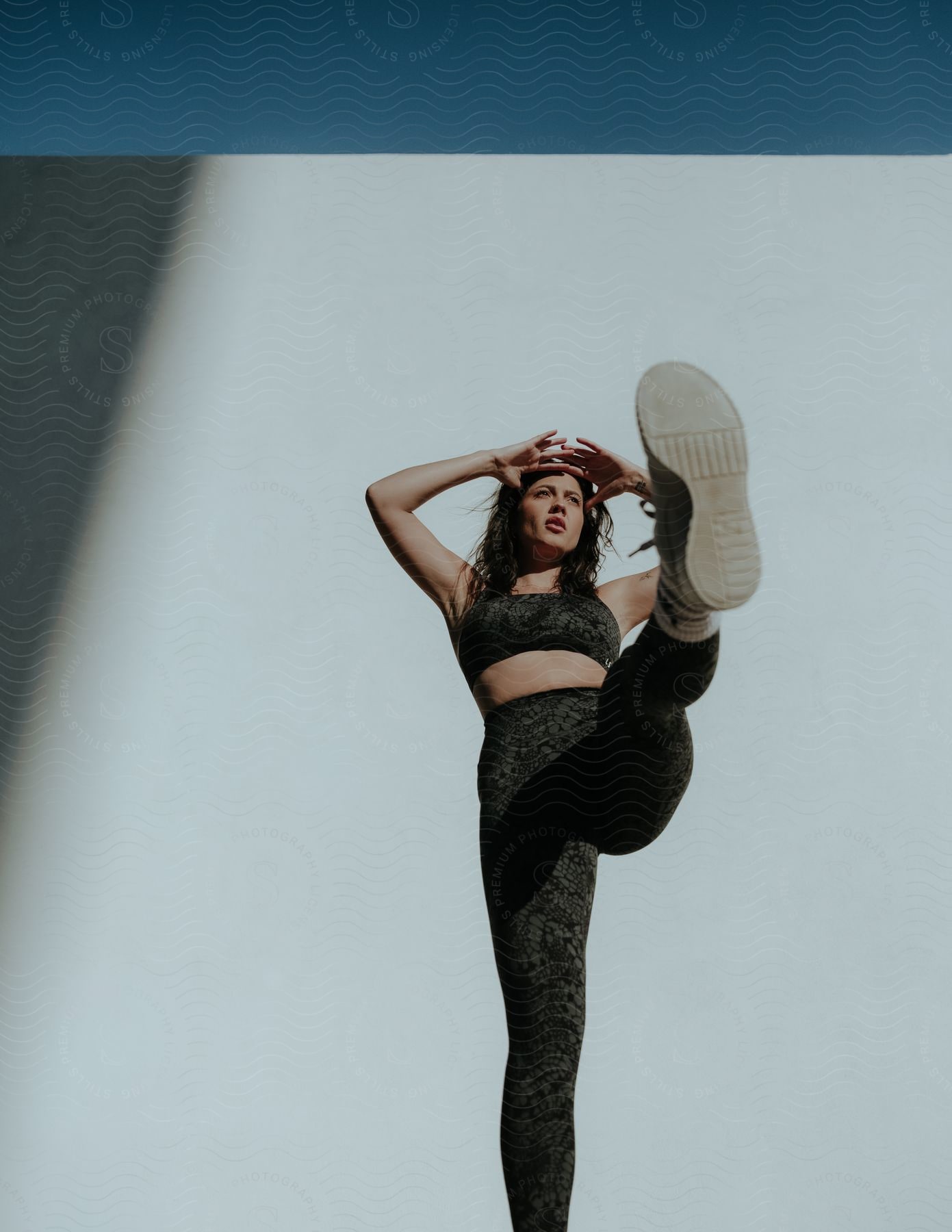 A young lady poses in a studio wearing leggings and a crop top raising one leg gracefully during a photoshoot