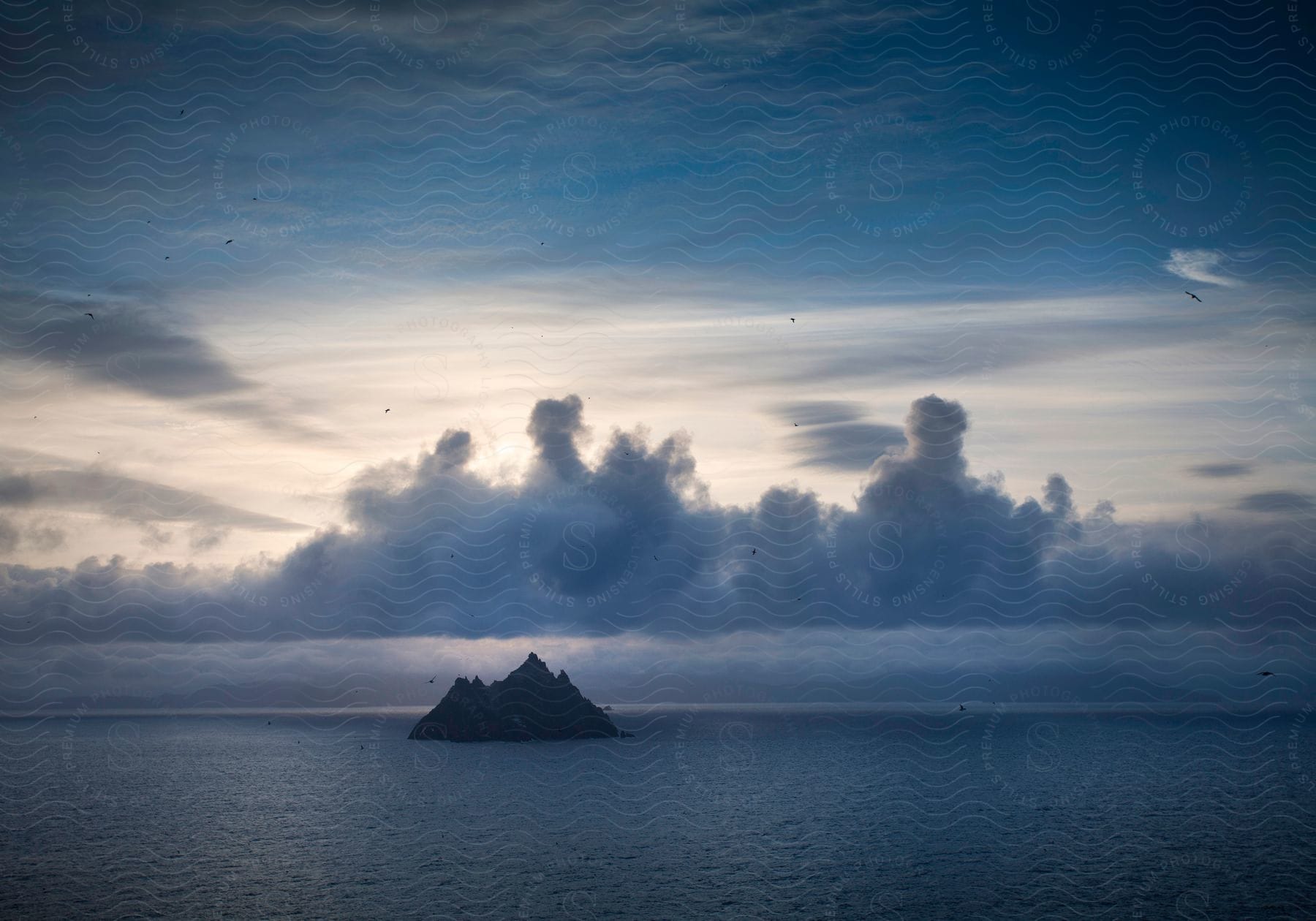 Birds flying over water around a mountain island under a cloudy sky