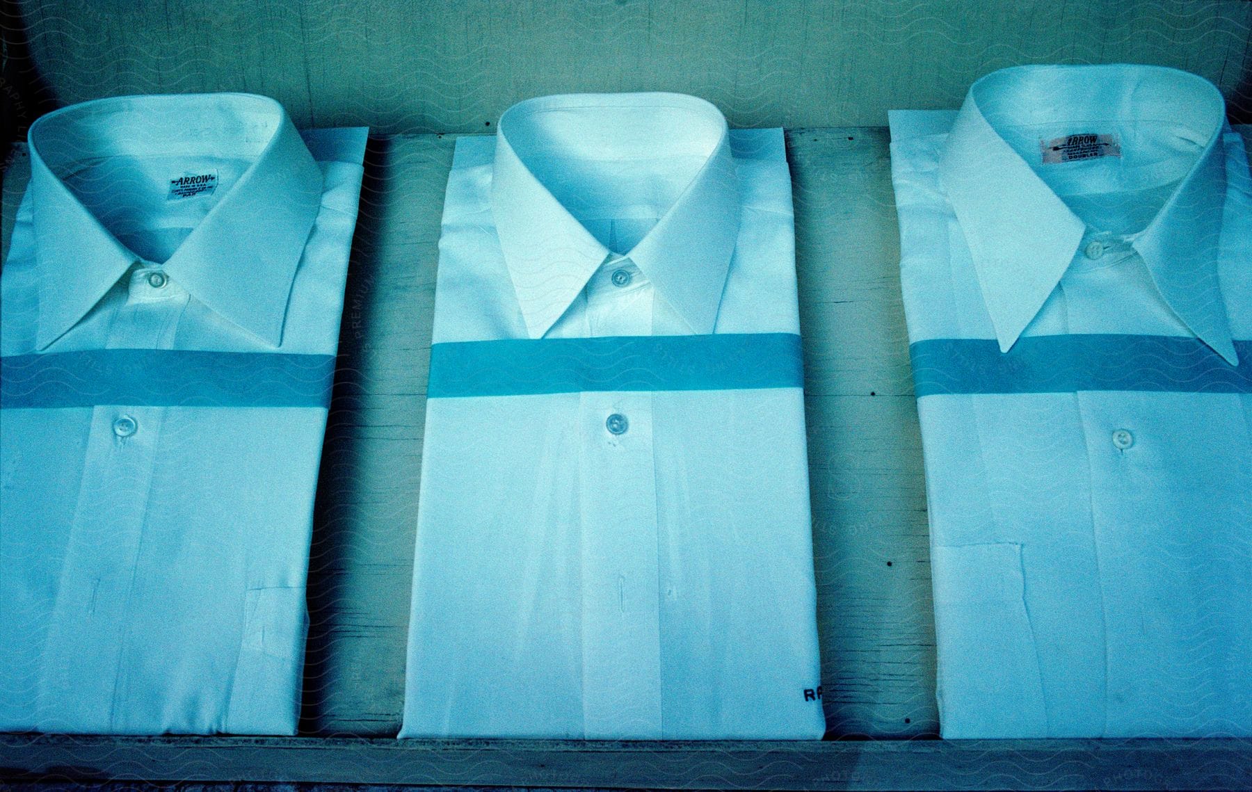 Three folded dress shirts on a wooden shelf