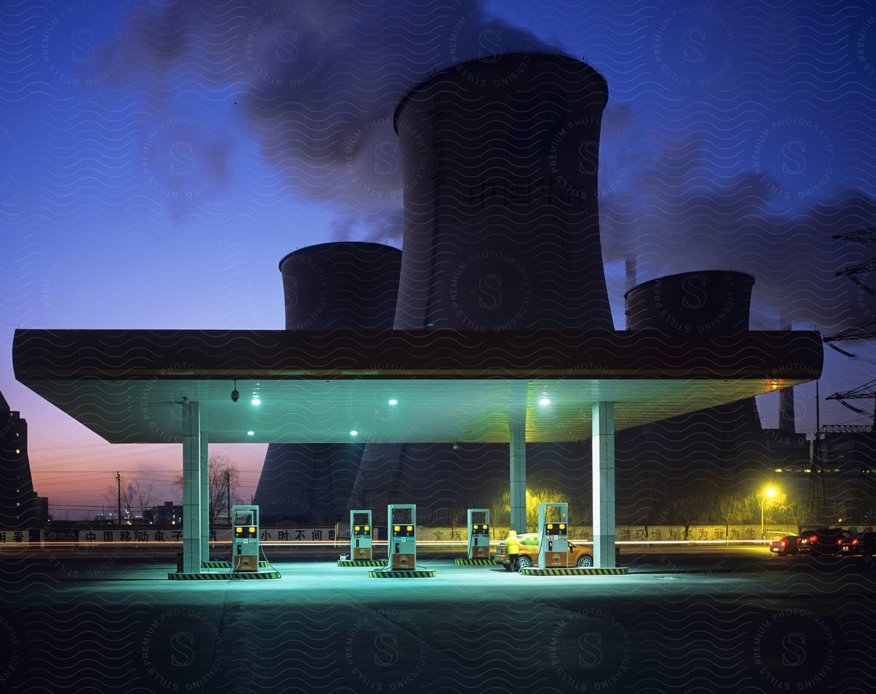 A gas station is seen next to cooling towers on a plant at night time