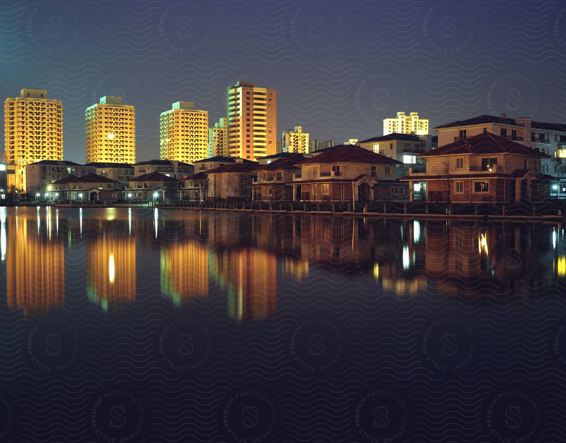 A city skyline at dusk with buildings reflected in a lake