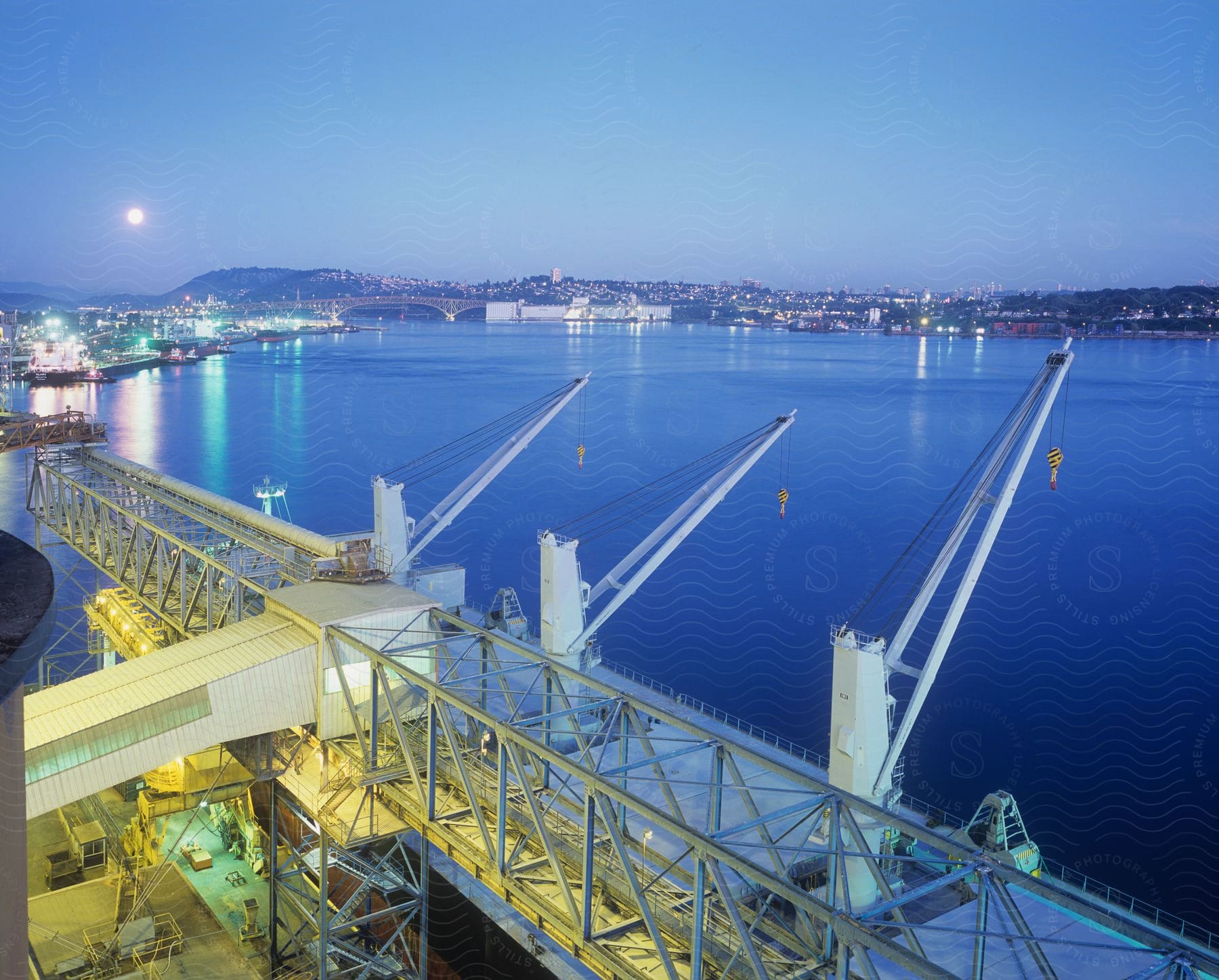 A crane overlooks a moonlit port at night with the city skyline fading into the horizon