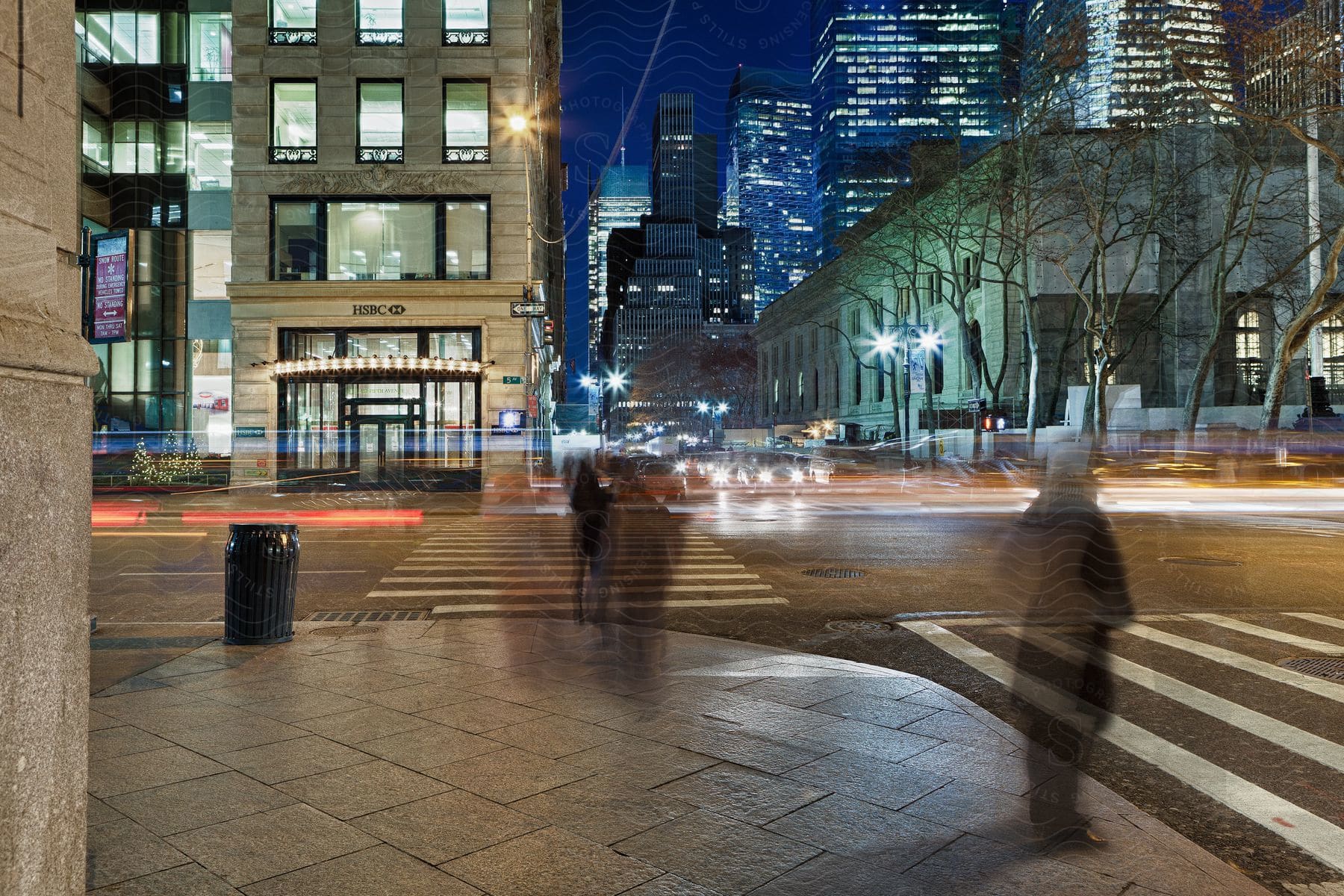 Traffic and pedestrians on a city street at night near illuminated buildings