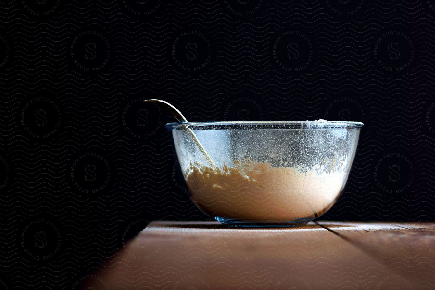 A metal spoon rests in a glass bowl with flour in it