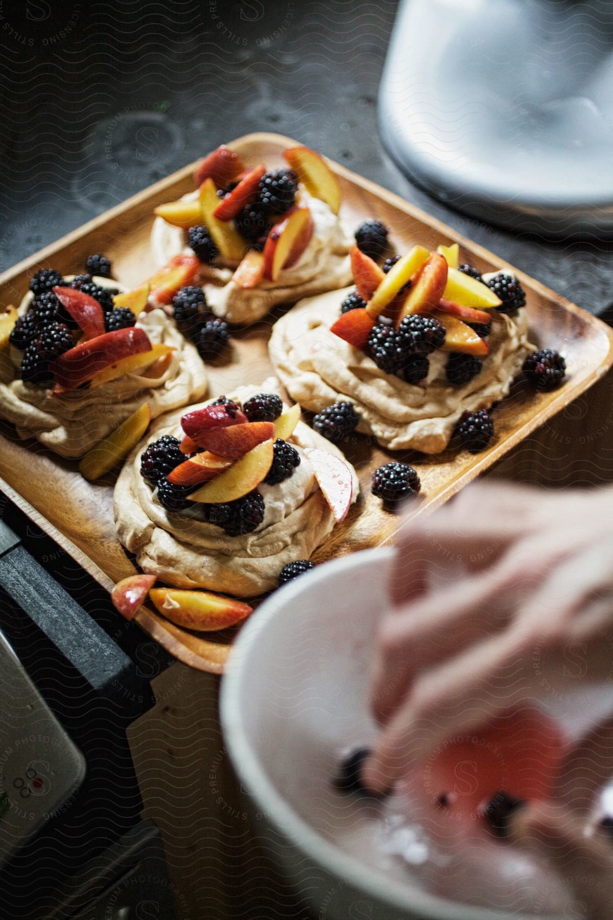 A person prepares a platter of appetizers adorned with blackberries and fruits