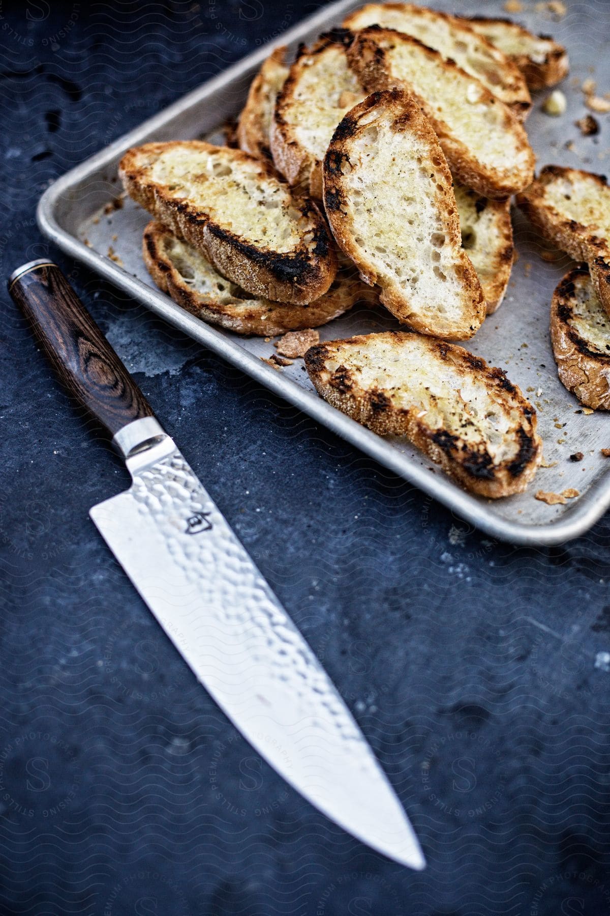 Sliced baked bread is on a baking sheet next to a knife