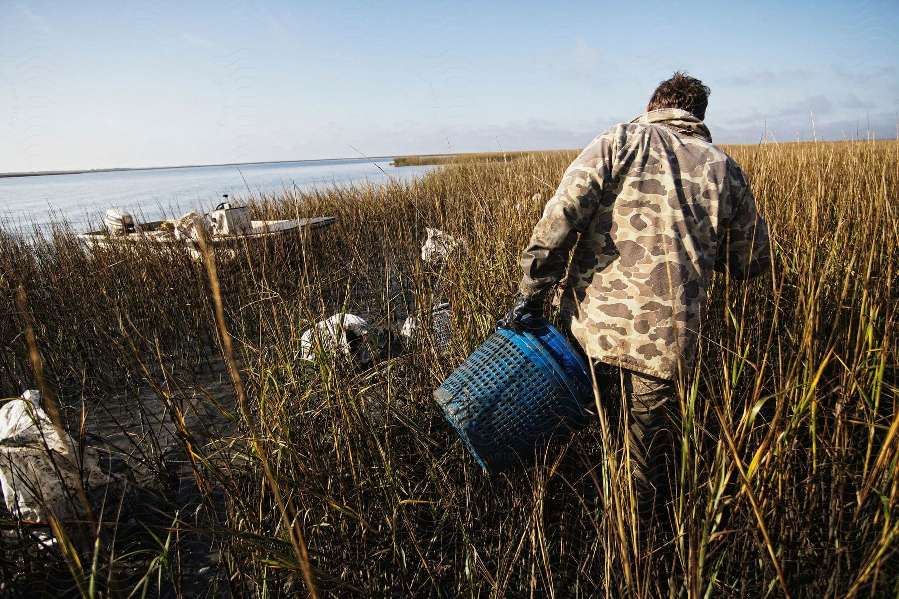 A man holding a basket walking through a grassy land with a sea at his left side