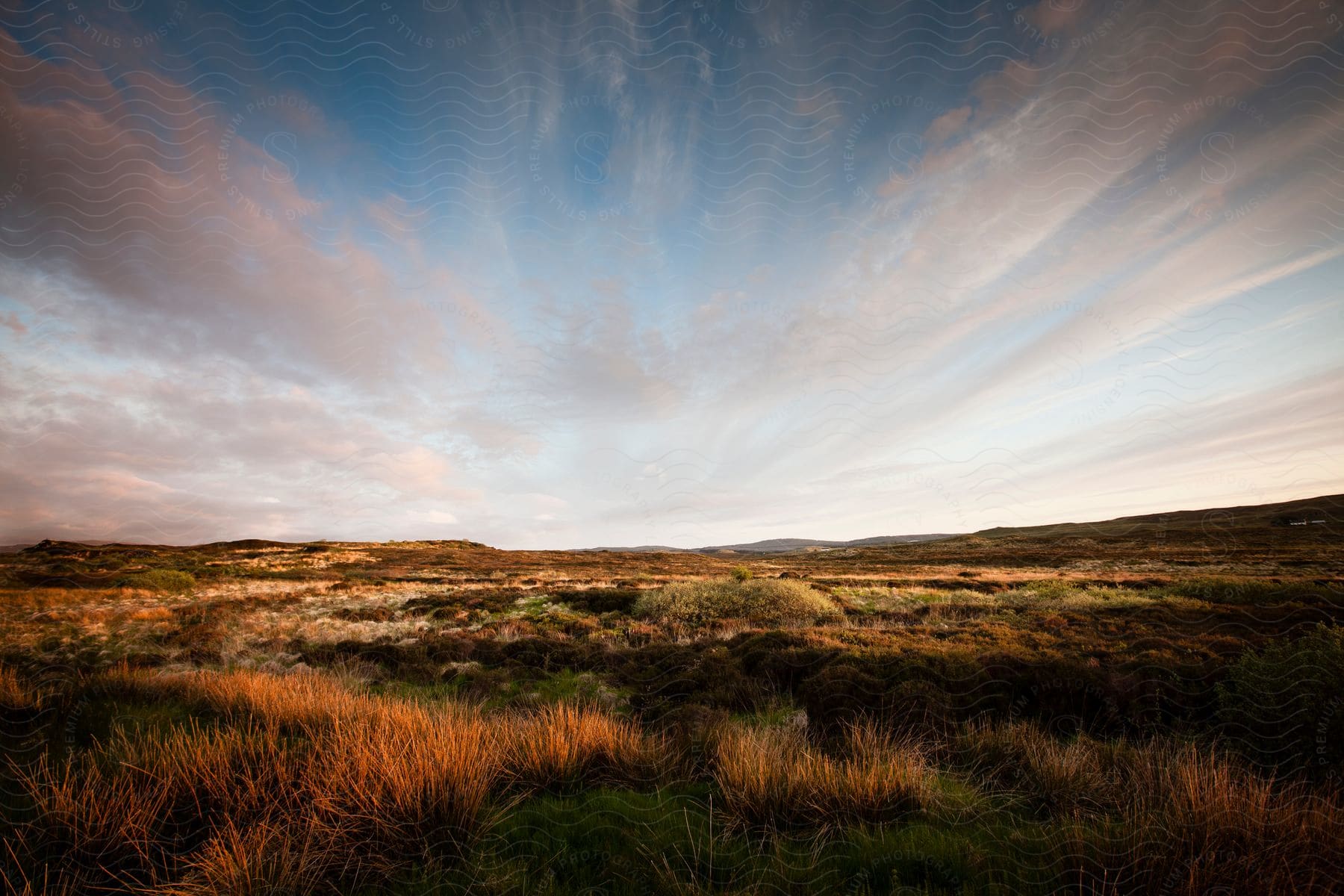 Clouds and grass covered plains stretch to the mountains on the horizon