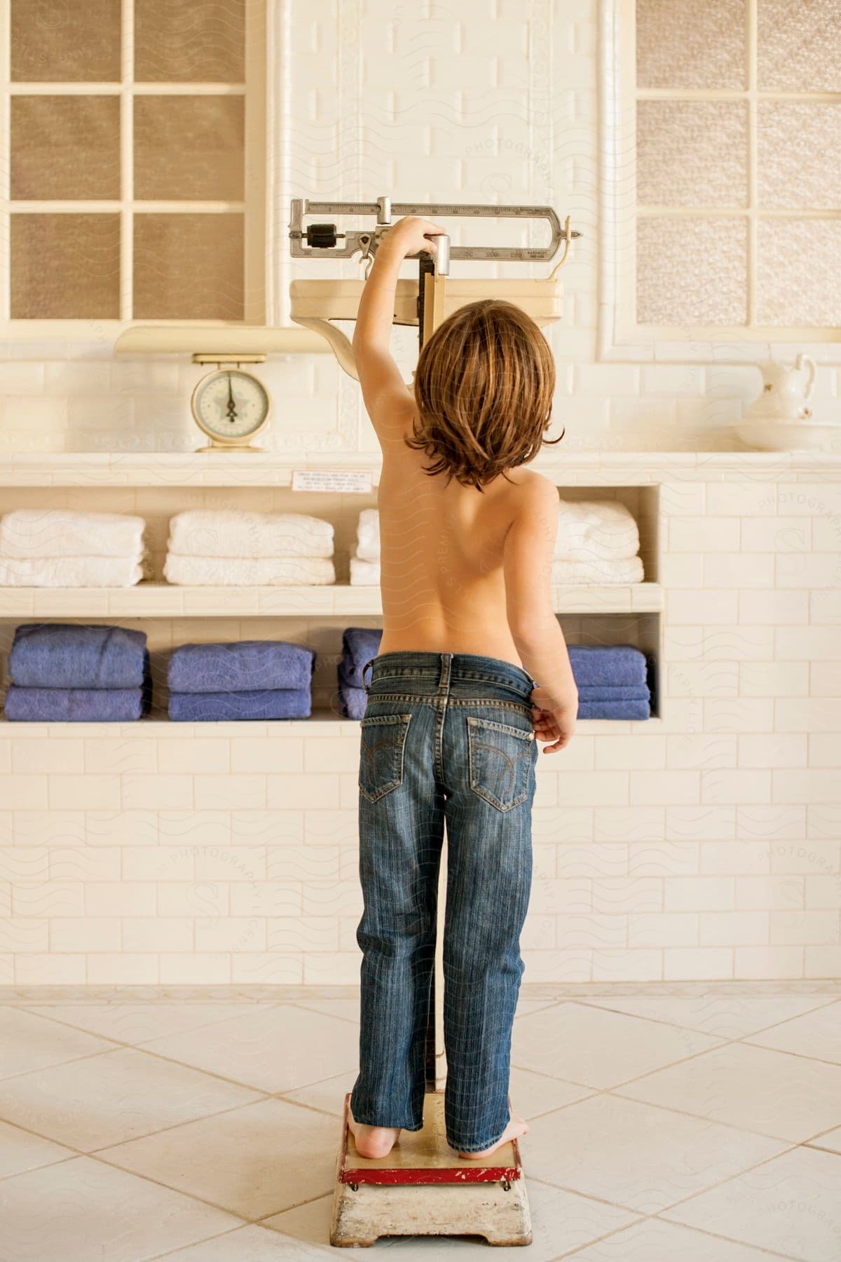 A boy weighing himself on a mechanical beam scale in a white tiled bathroom