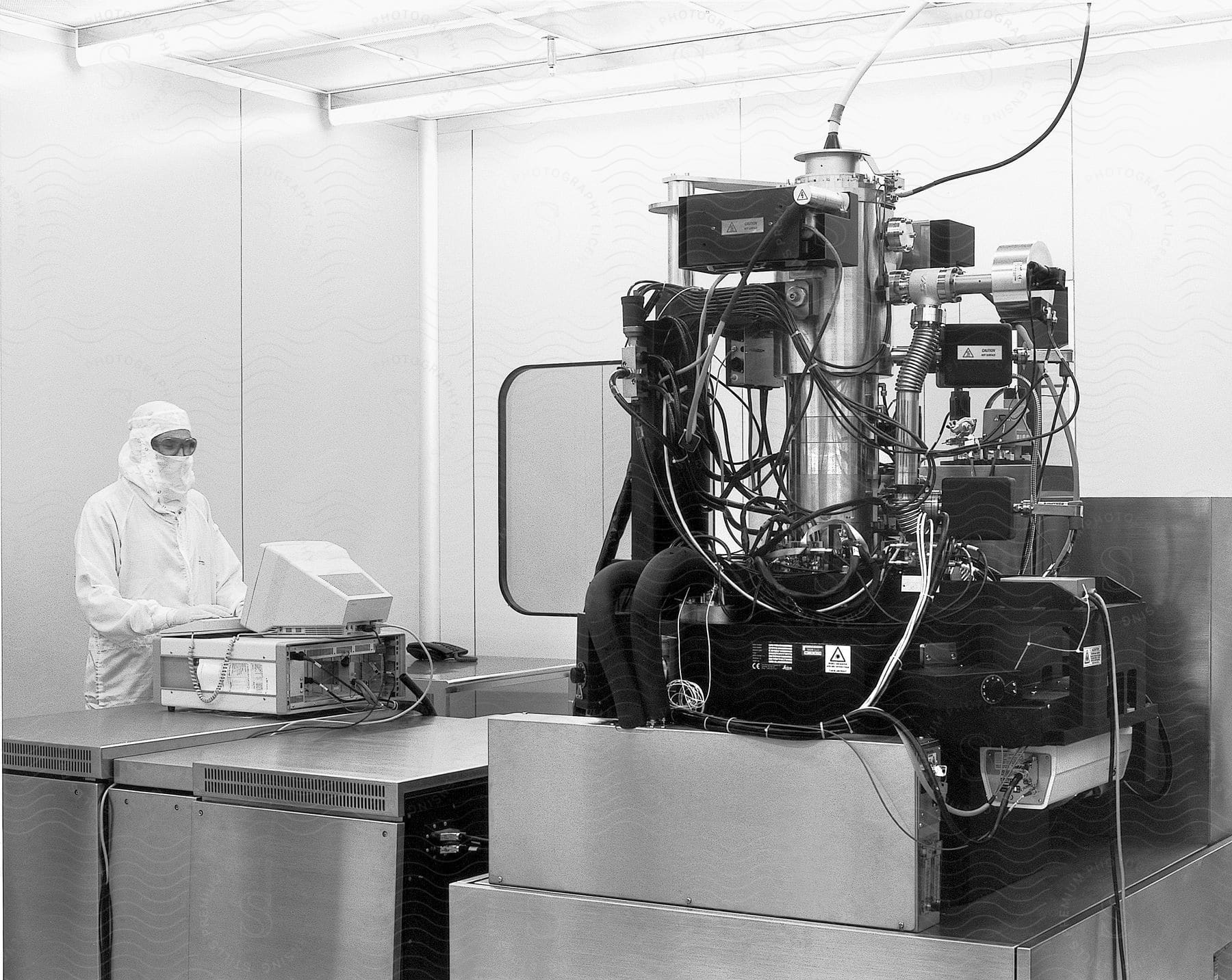 A person in a hazmat suit is seen in a lab with a large mechanical device standing in front of a computer