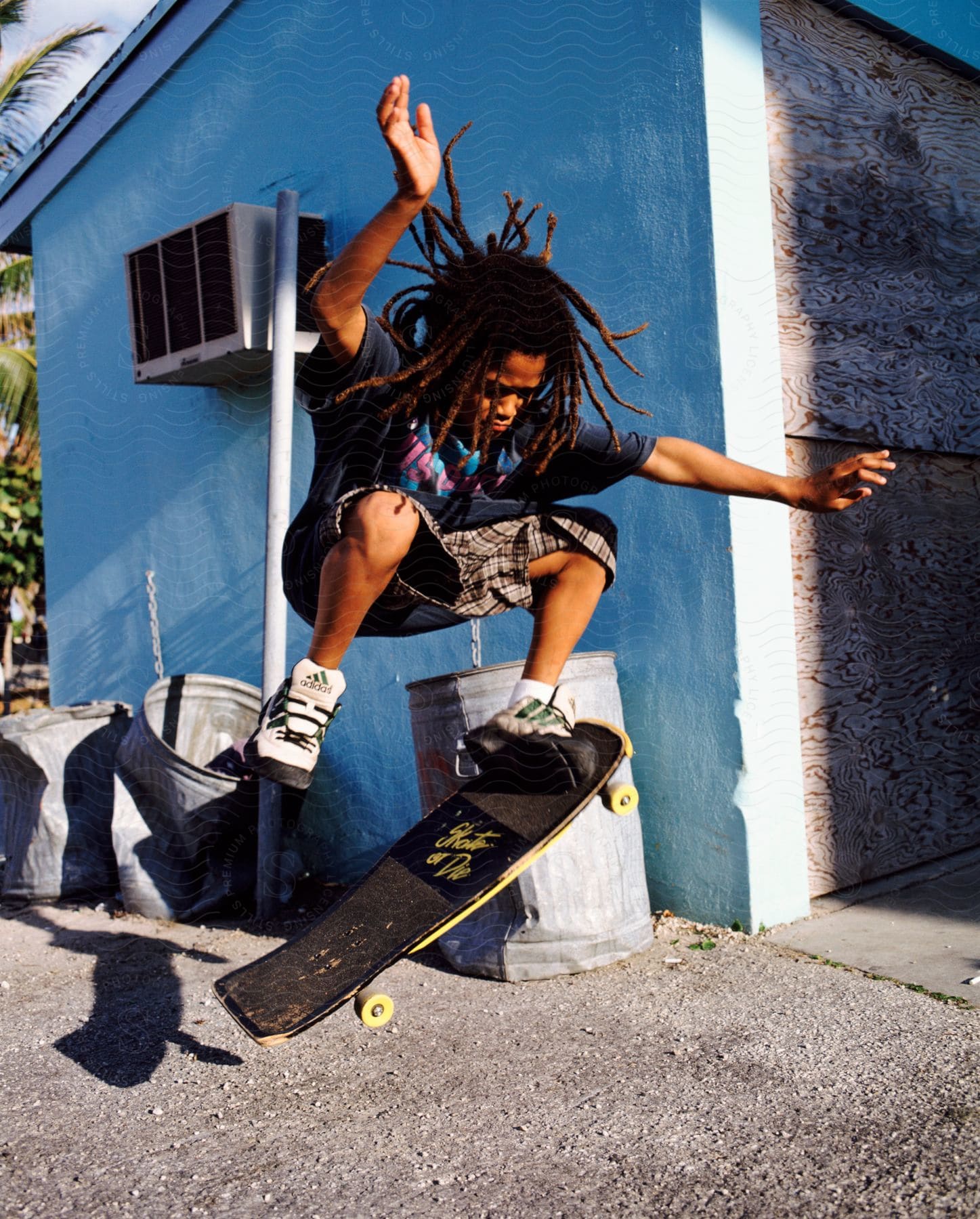 A skater performing a jump in front of a blue wall and several dented trash cans