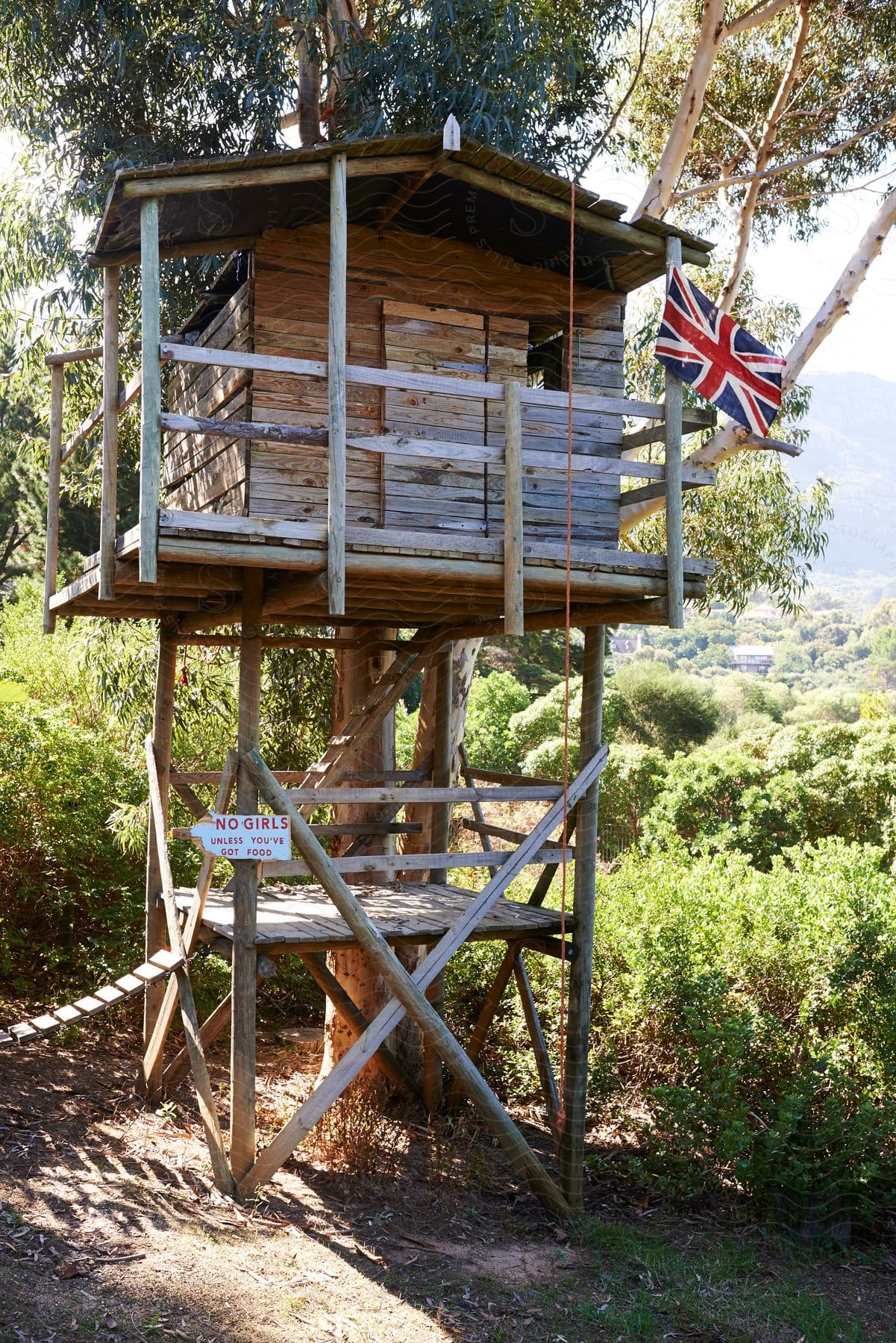 A wooden playhouse tower next to a tree with a british flag