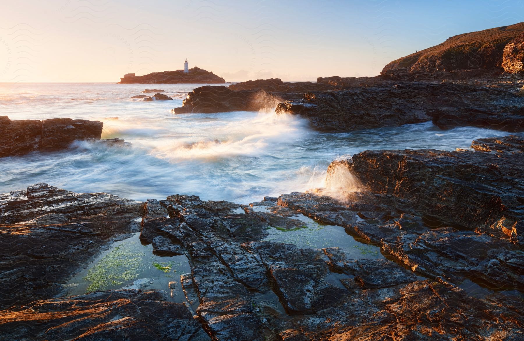 Sunset view of godrevy lighthouse across rocky coast