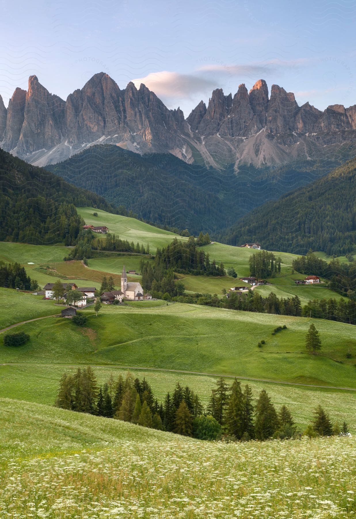 A green field with farmhouses mountains forests and hills illuminated by a sunset