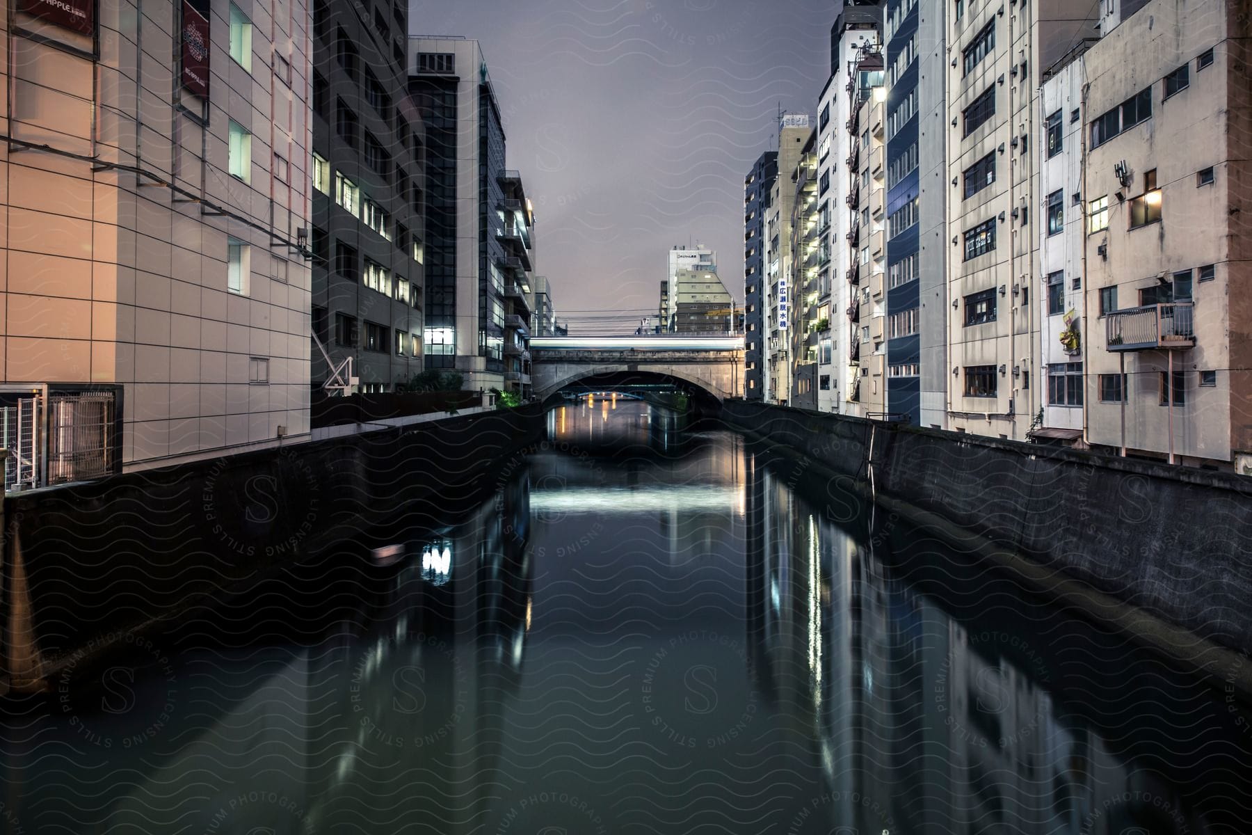 A River Flows Between Tall Apartment Buildings At Night In A City