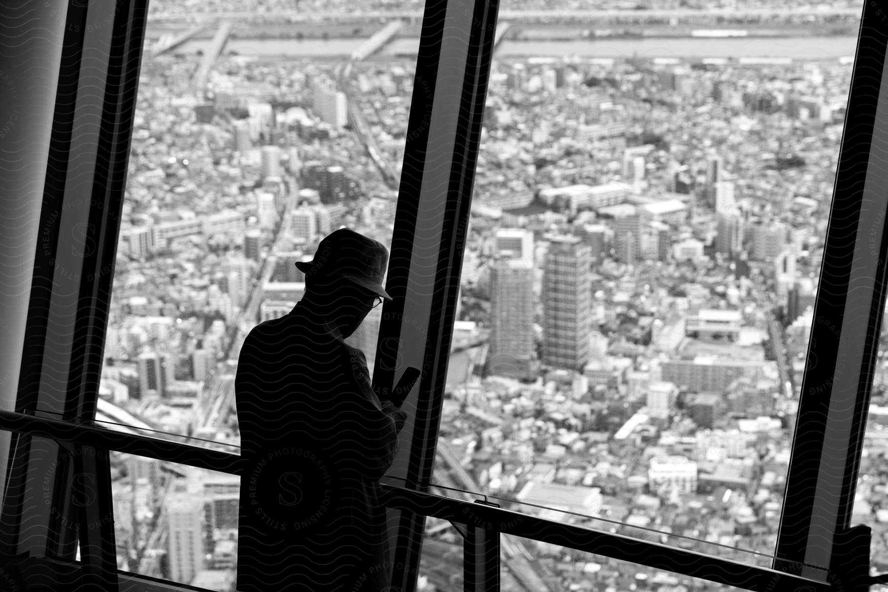 A person in a hat and overcoat is seen against city buildings from an observation deck