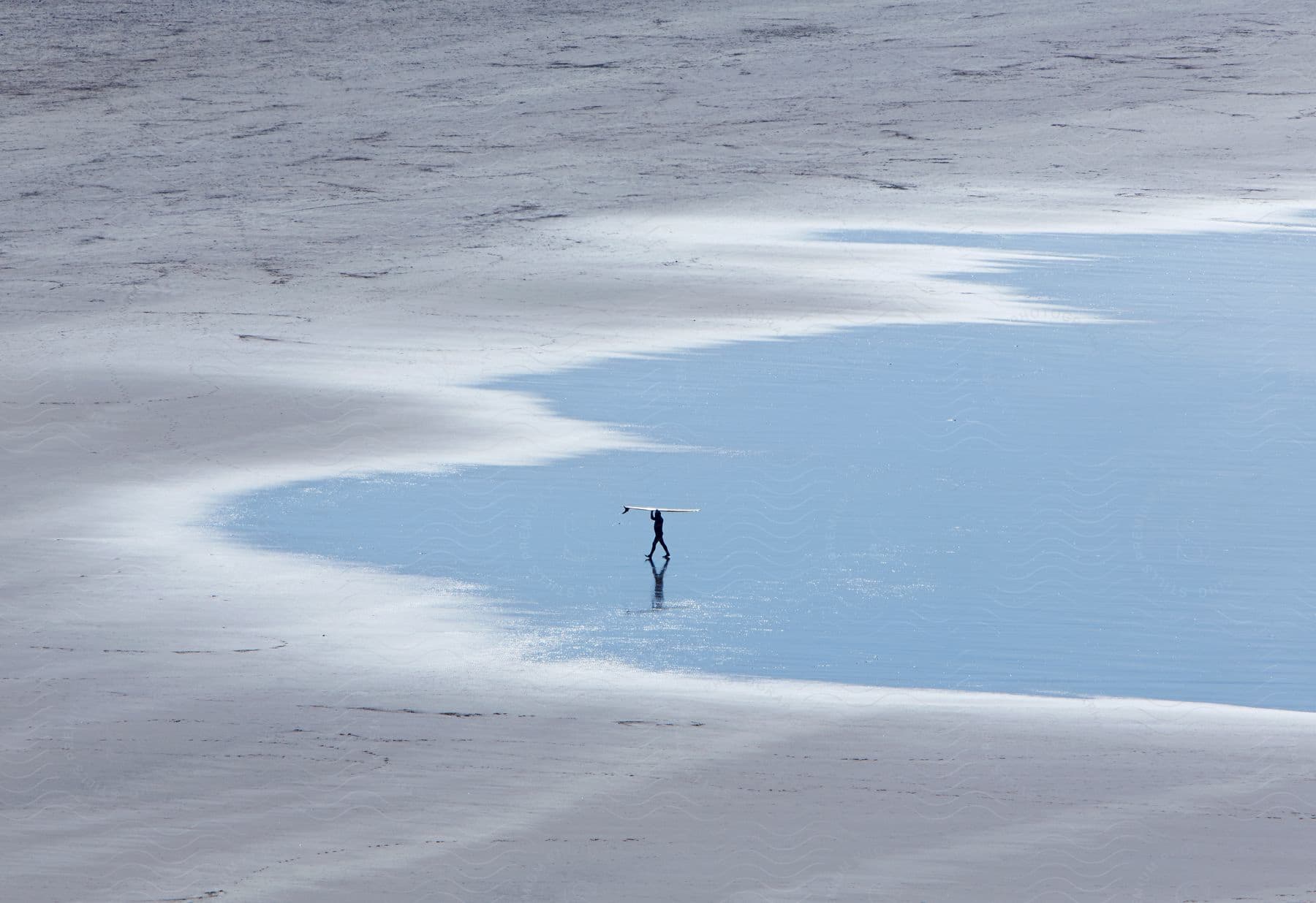 A person walking on the beach carrying a surfboard over their head during the day