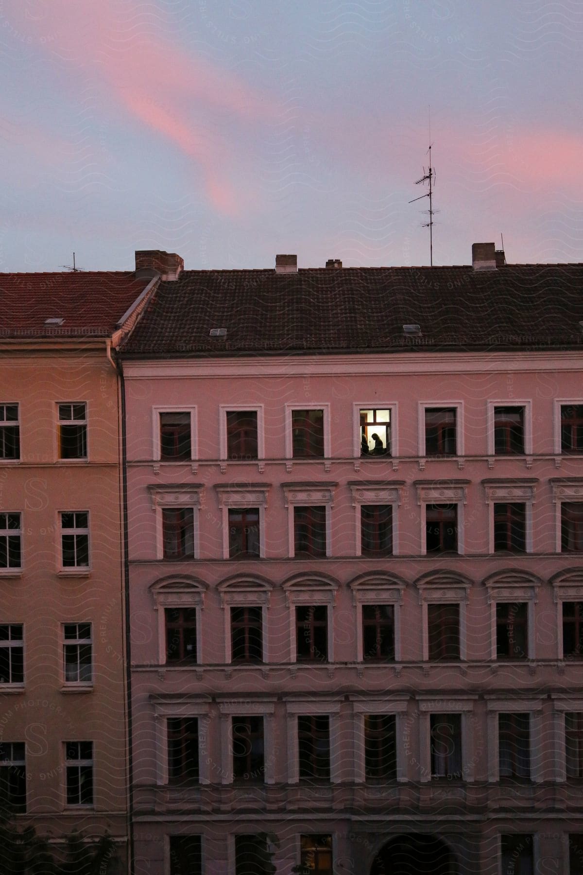 Colorful apartment buildings with lots of windows in a berlin building style with two girls in a lit open upstairs window at sundown