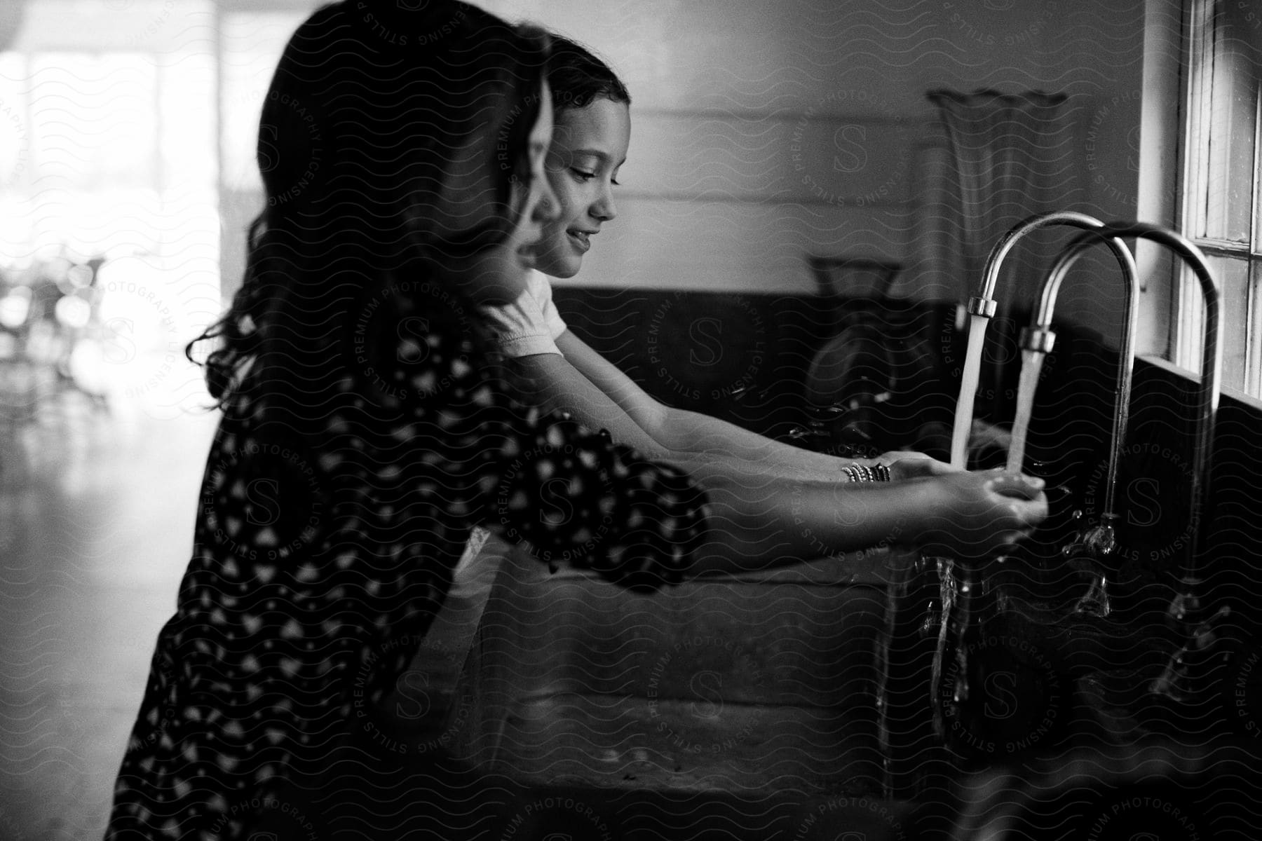 A mother and daughter are washing their hands together at the kitchen sink