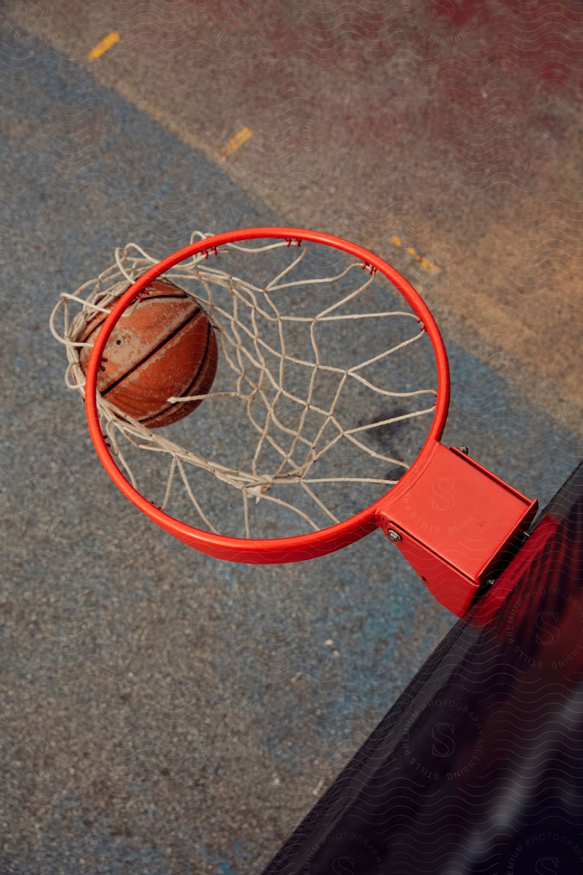 A basketball falling through a net on a hoop on an outdoor court