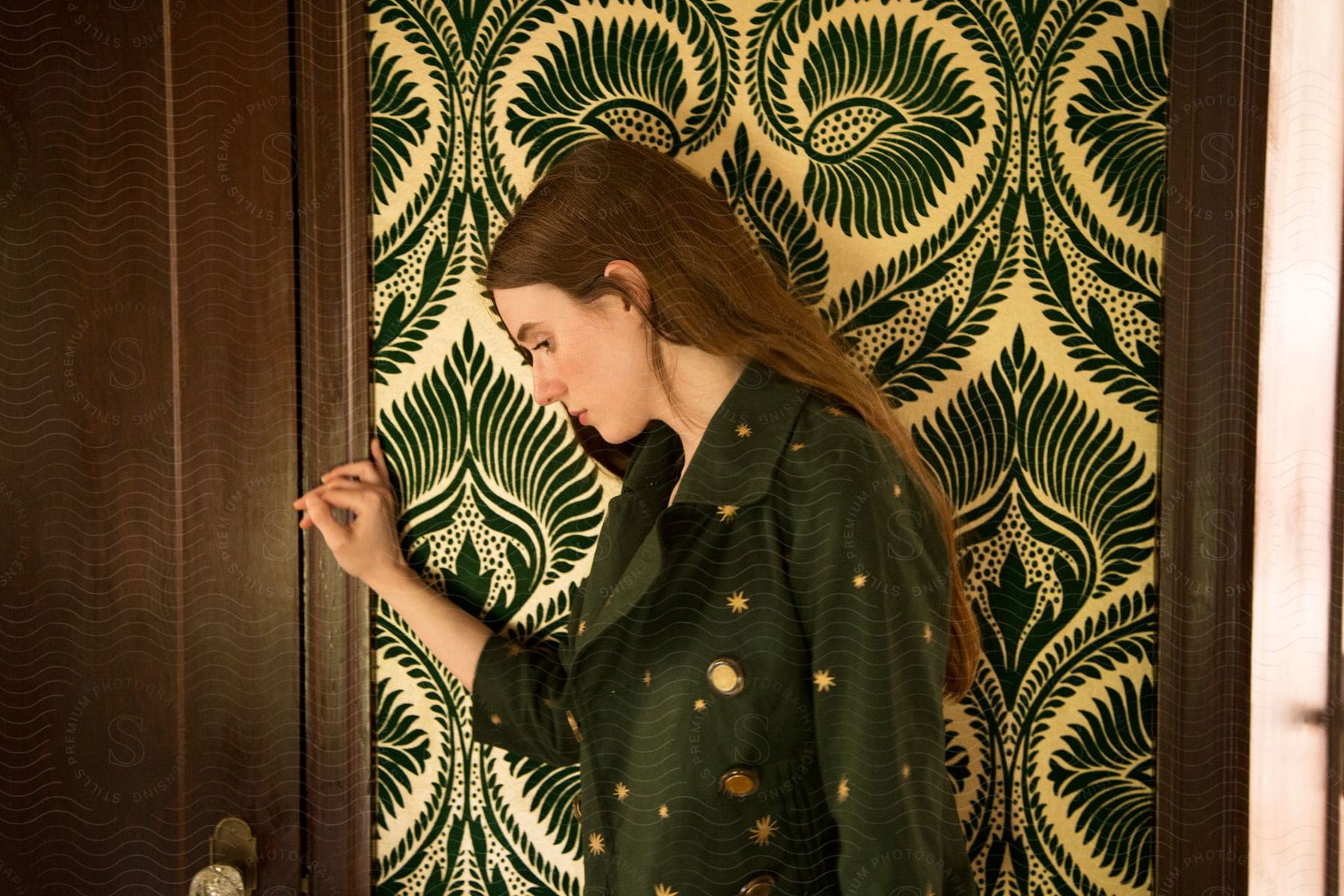 A young woman stands next to a wallpaper seen from the side