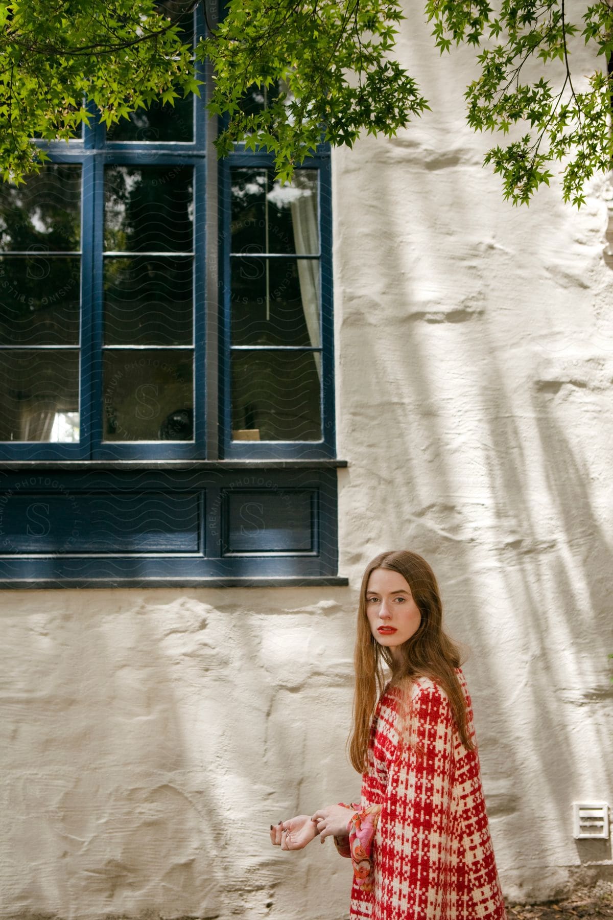 A woman stands near a window outside a building glancing back for a photo