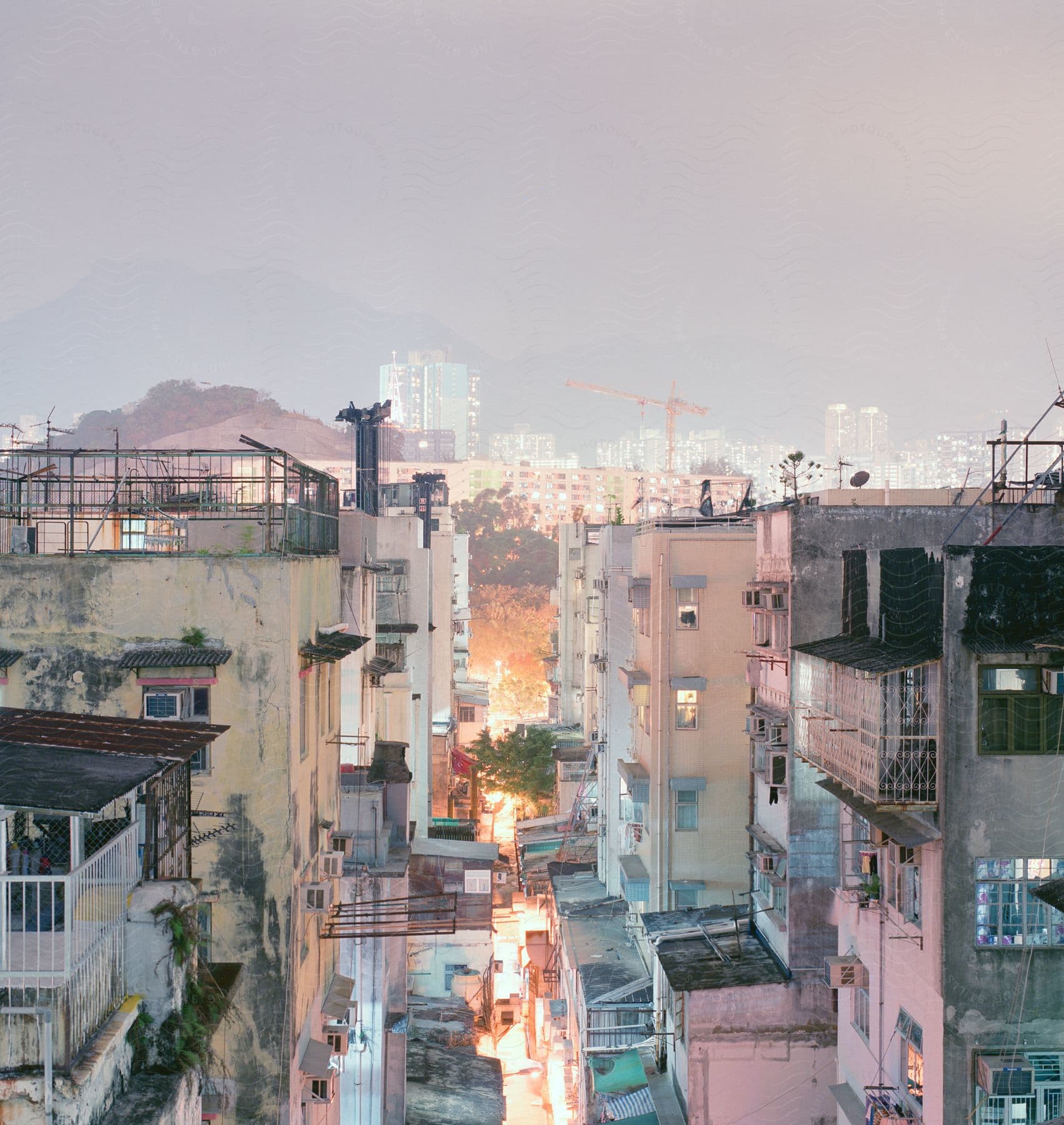 Brightly lit alley separates apartment building a distance from fog covered city