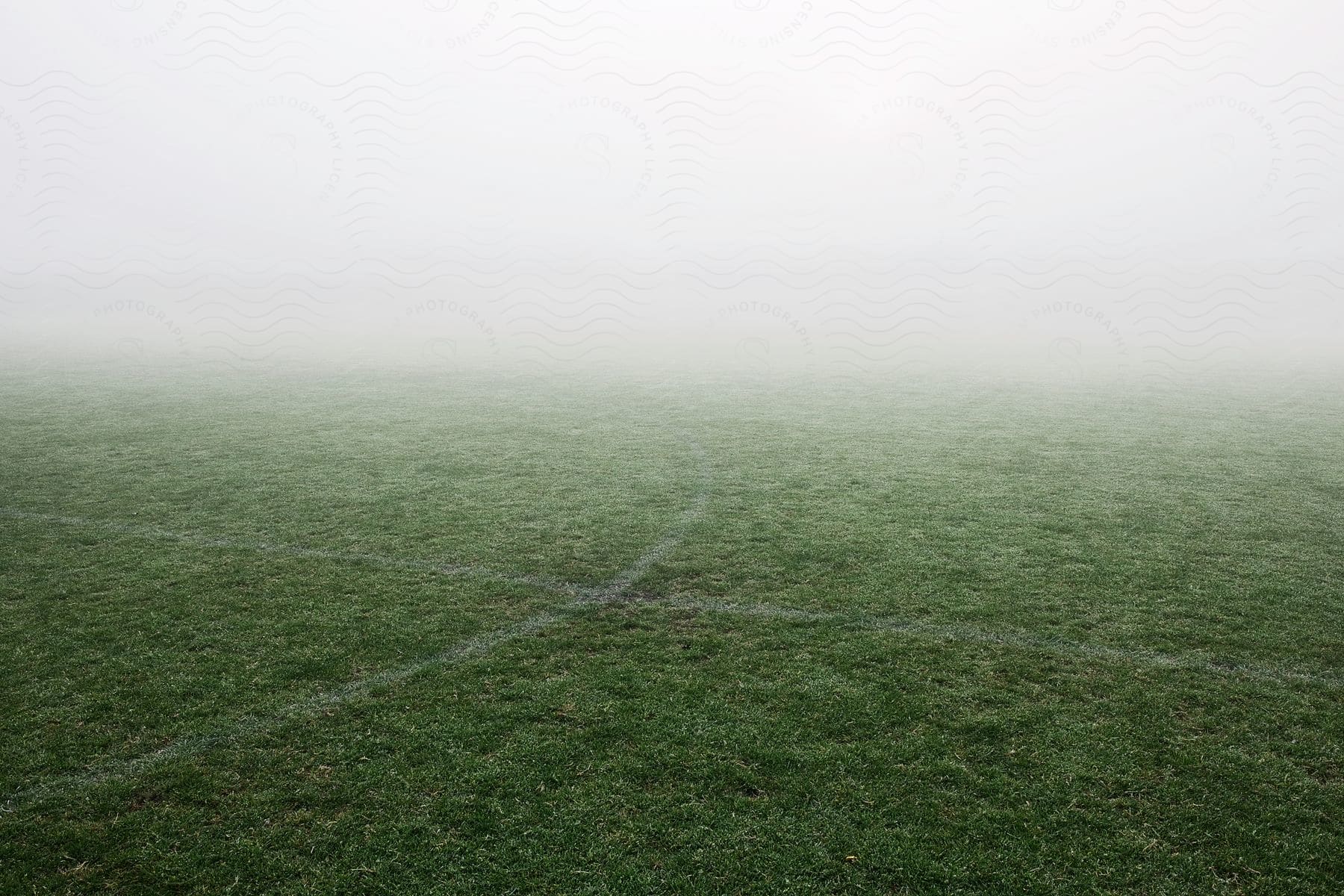 A foggy football field surrounded by grass and cloudy weather