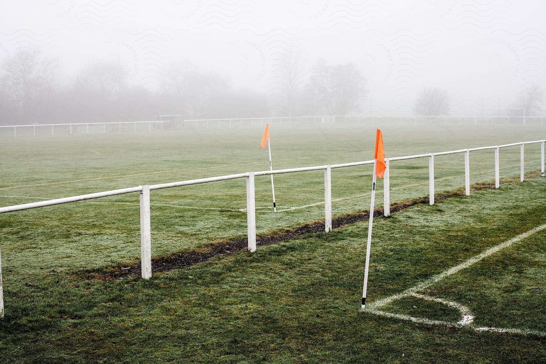 Two soccer fields separated by a fence one with a corner flag visible the other partially obscured by fog