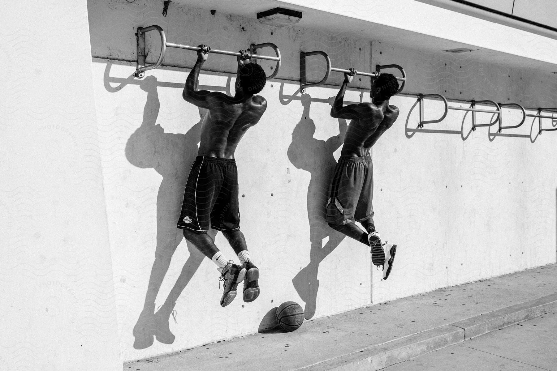 Two black men doing pullups side by side with a basketball on the floor