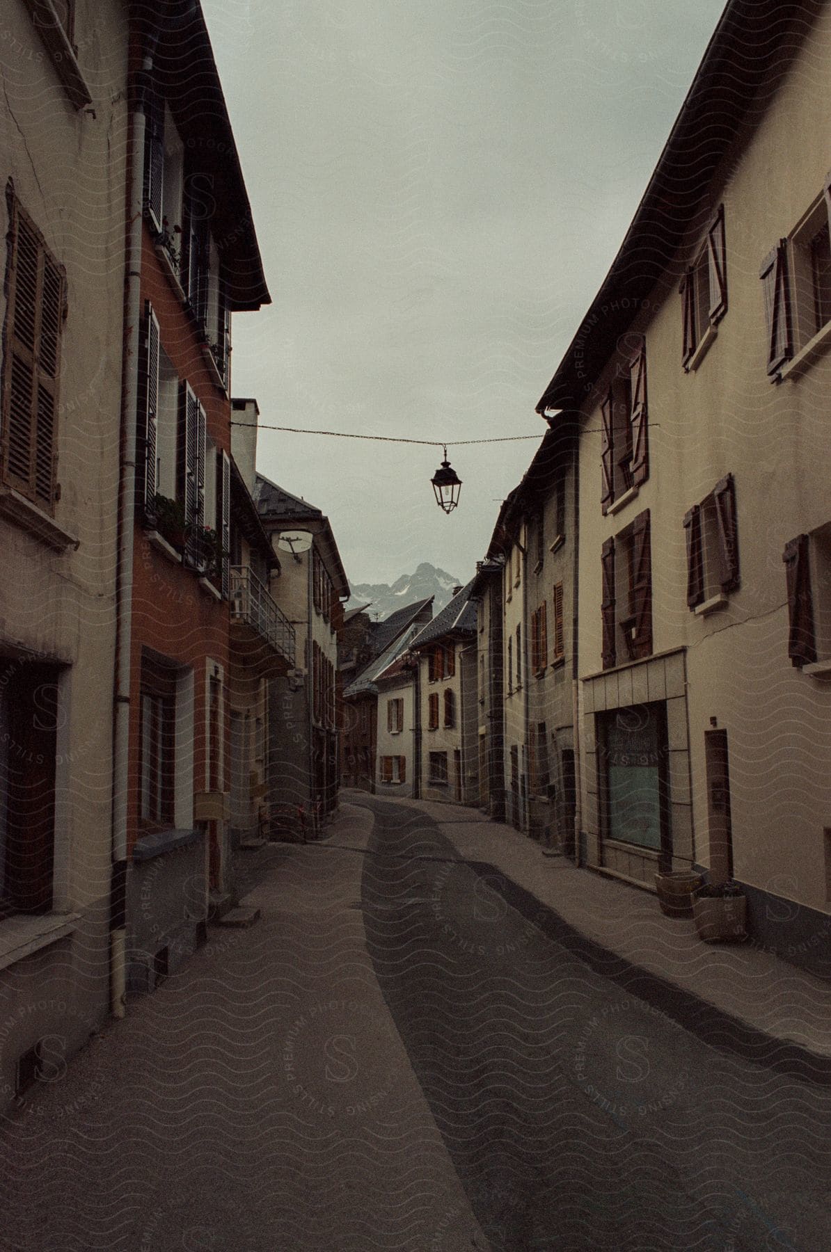 Brown facade buildings line a french alleyway with open shutter windows and a suspended street lantern