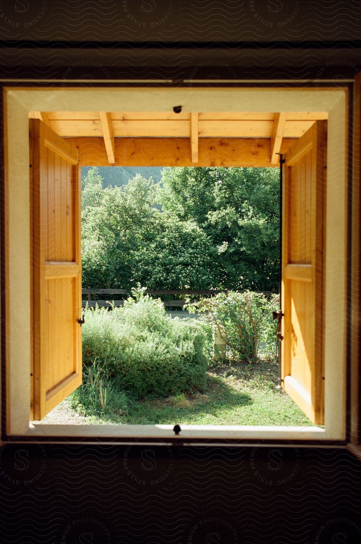 A cabin window reveals a grassy stretch and wooden fence with swaying tall grasses in the distance