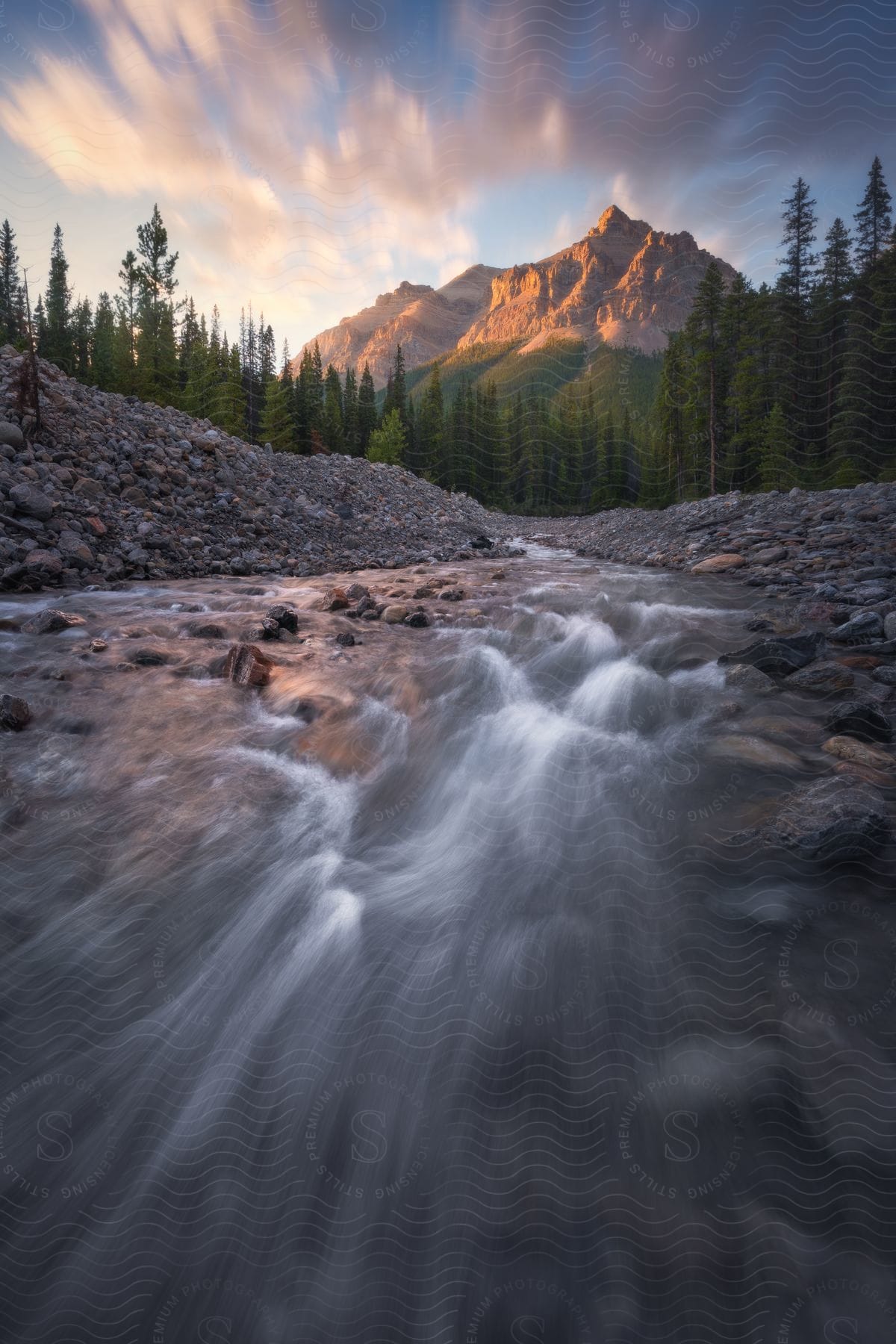A sunrise illuminating a rocky mountain peak with a stream in the foreground