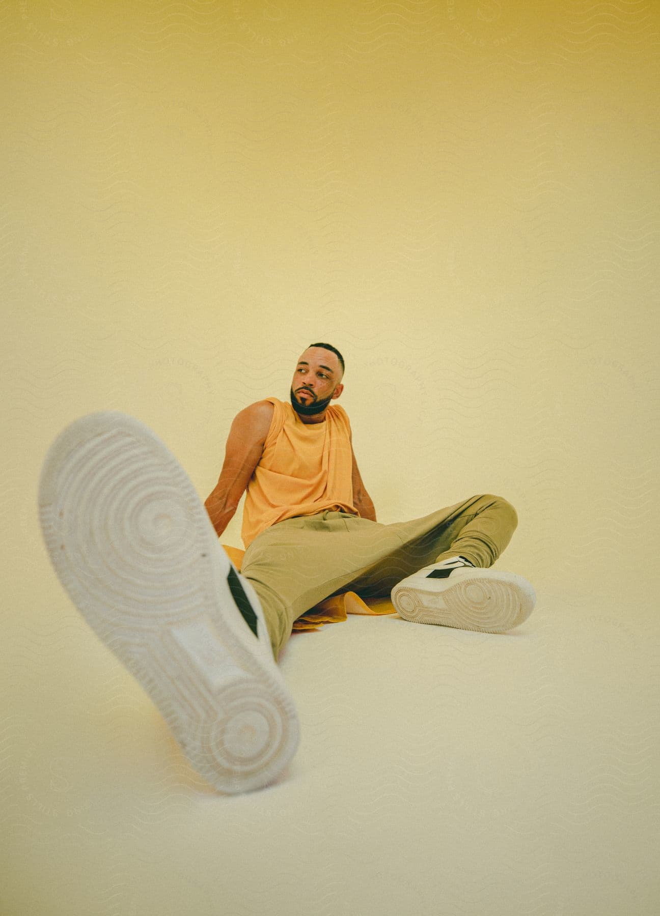 A man sitting on the floor posing with one shoe forward under yellow lights