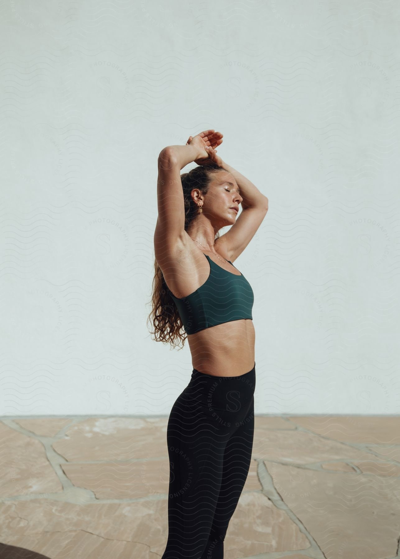 A woman in green sports bra and black leggings stretches upwards in a yoga pose