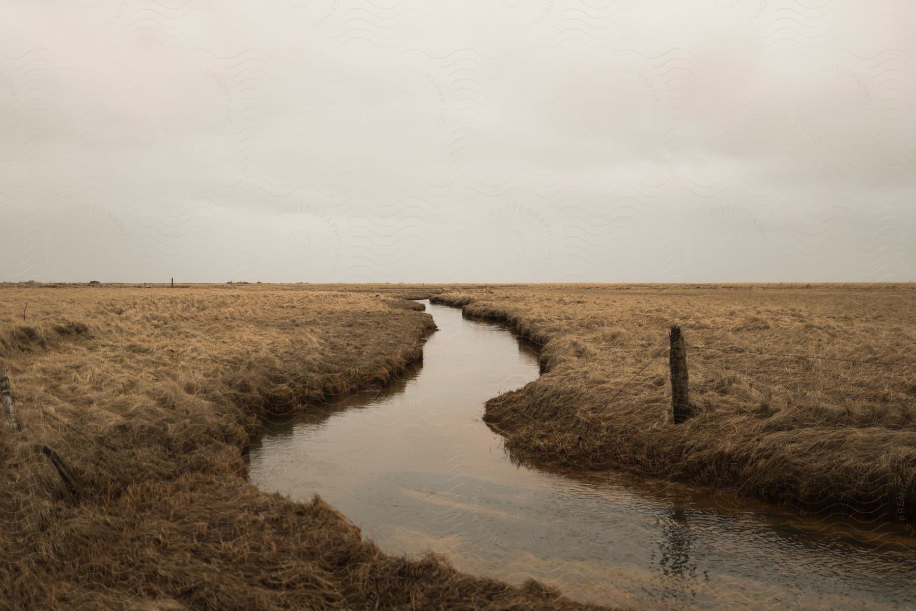 A stream flows through a dry field on a cloudy day providing relief to the parched landscape