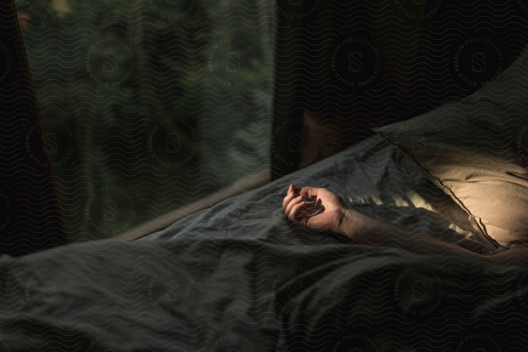 Soft light shines through a window onto a persons hand lying in bed