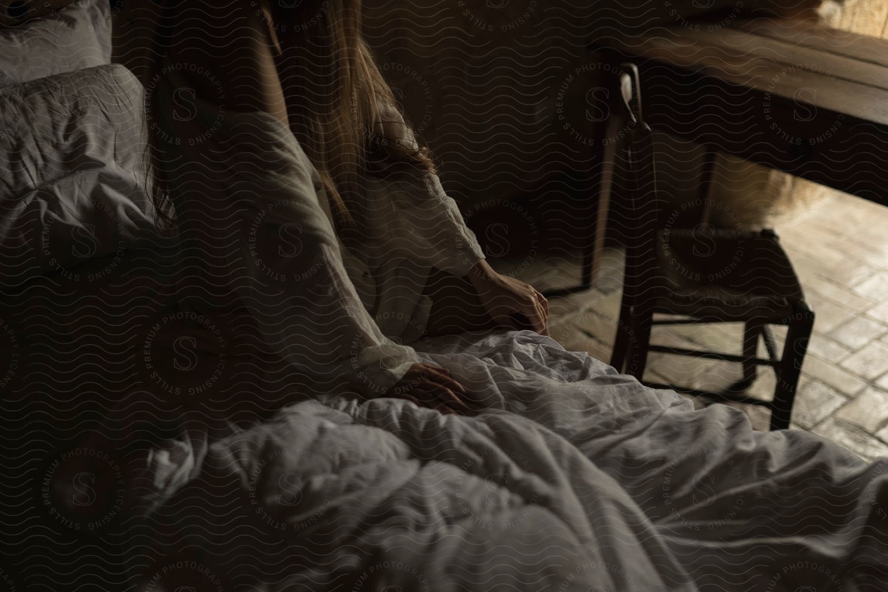 A person is sitting on a wooden floor near a window with a blanket draped over them